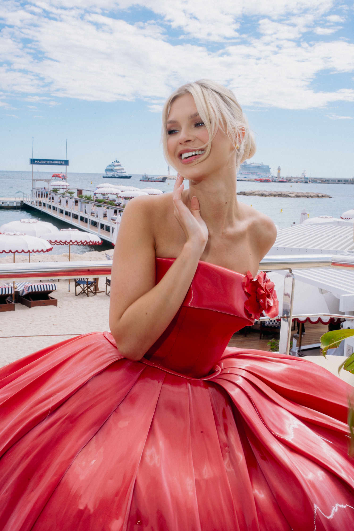 Stunning red ballgown photographed against a bright blue sky and beach backdrop.