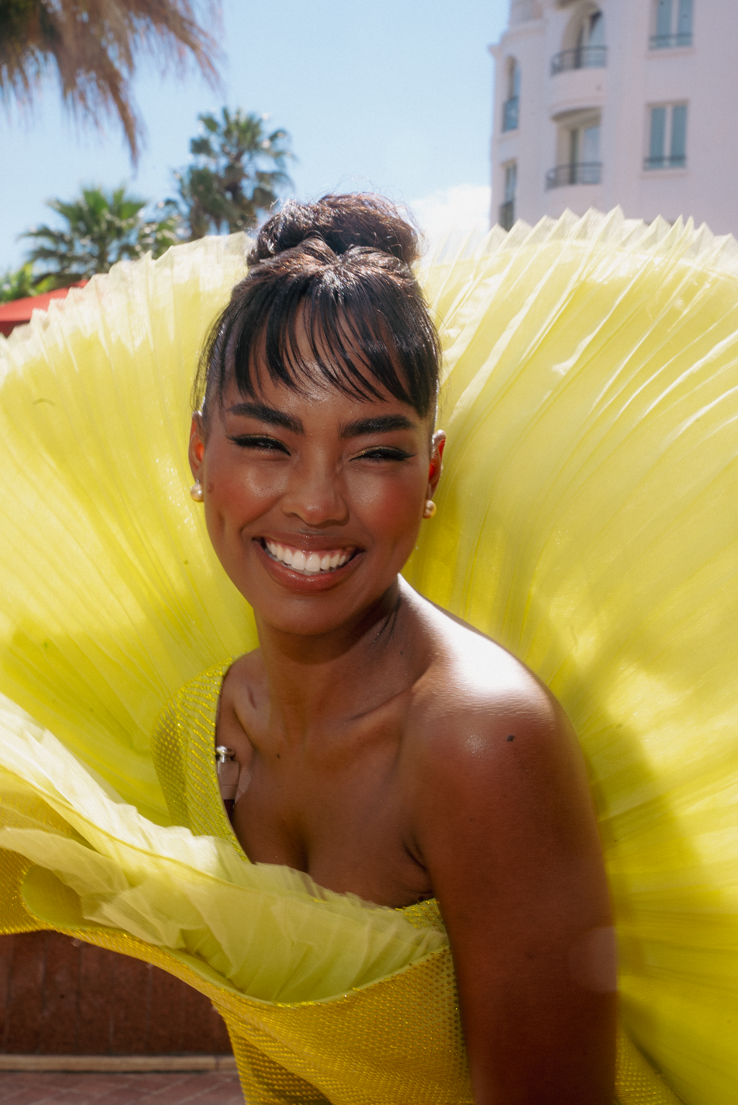 Model poses with vibrant yellow fan against tropical resort backdrop.
