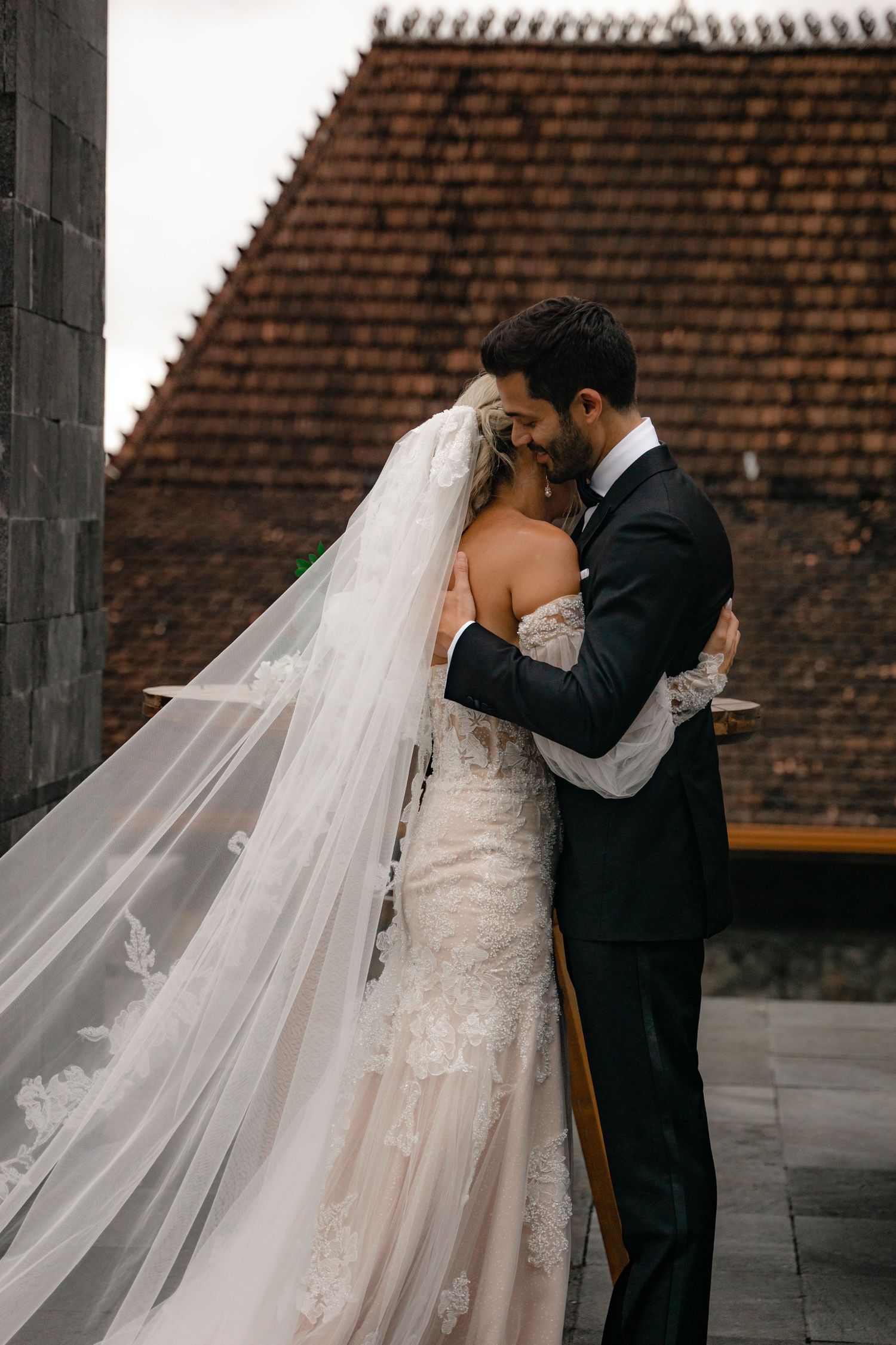 A romantic wedding couple shares an intimate moment against a terracotta tiled roof backdrop.