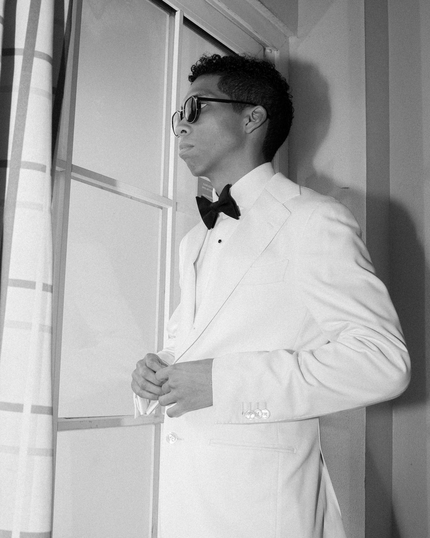 Close-up shots of groom adjusting bowtie in white tuxedo jacket.