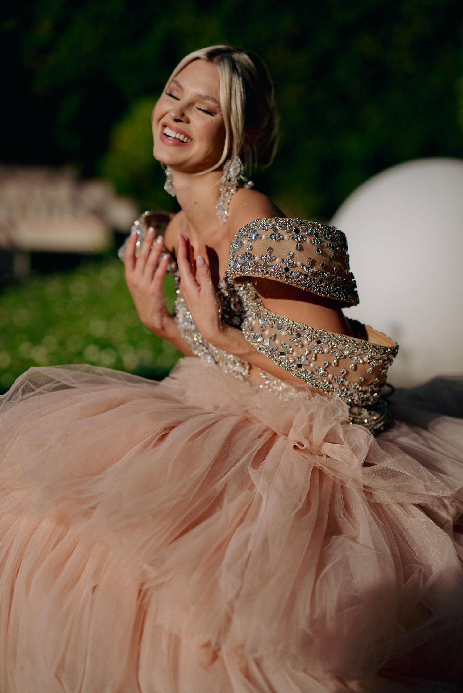 Elegant pose in flowing blush pink gown with crystal embellishments.