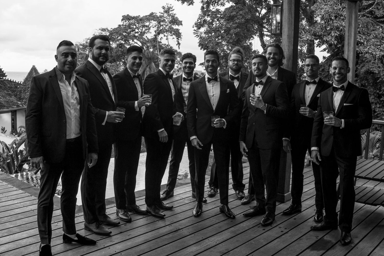 Large group of groomsmen in black tuxedos lined up for a formal wedding photo.