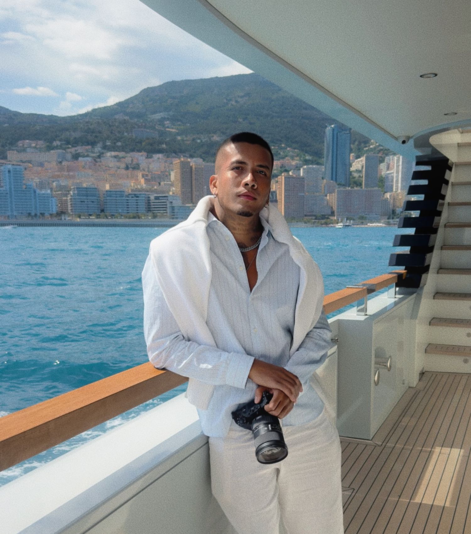 Person in white outfit cleaning yacht deck with coastal backdrop.