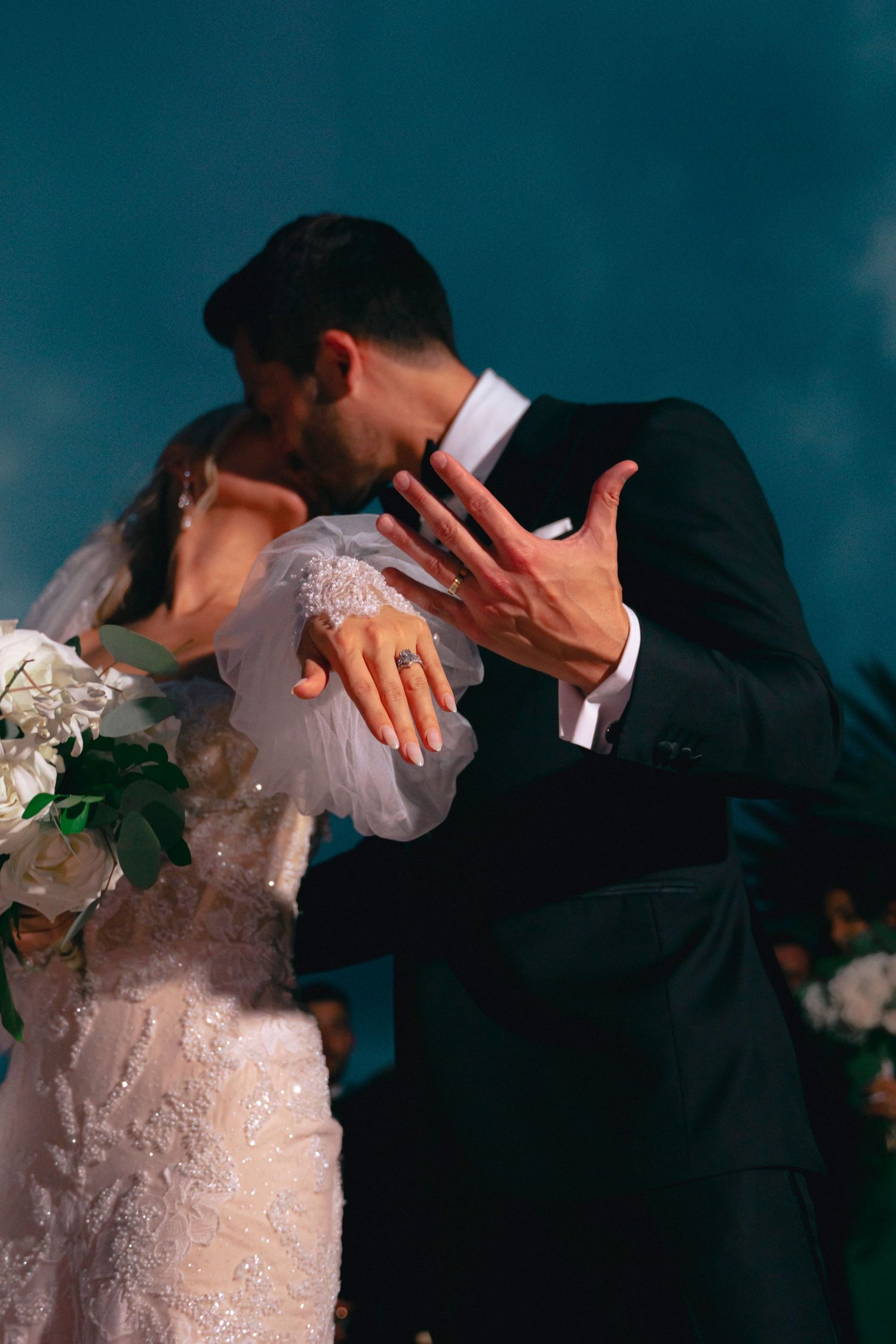 Close-up of a bride in a white lace dress embracing someone in formal attire during a wedding celebration.