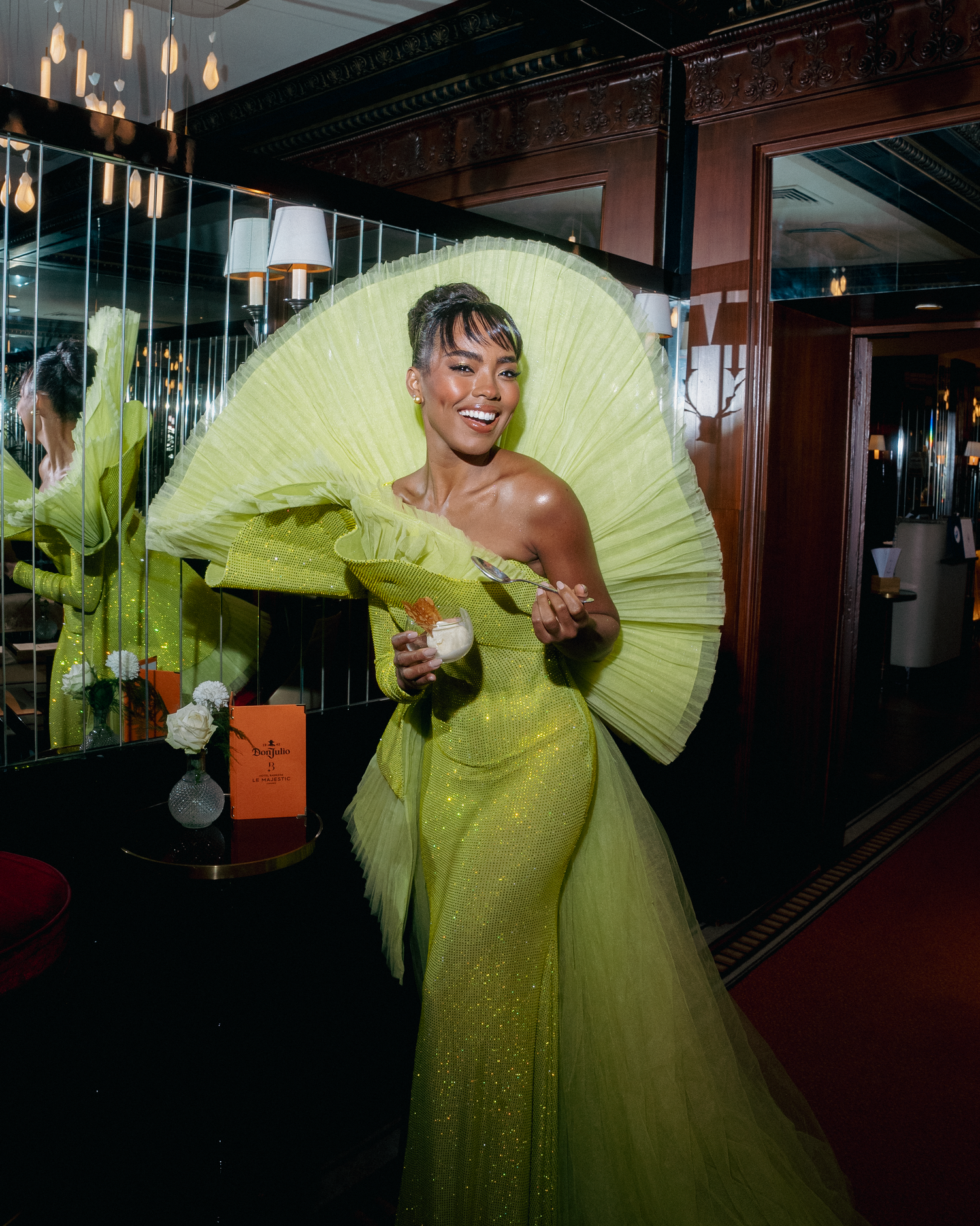 Energetic fashion shoot featuring lime green pleated gown in dimly lit indoor setting.