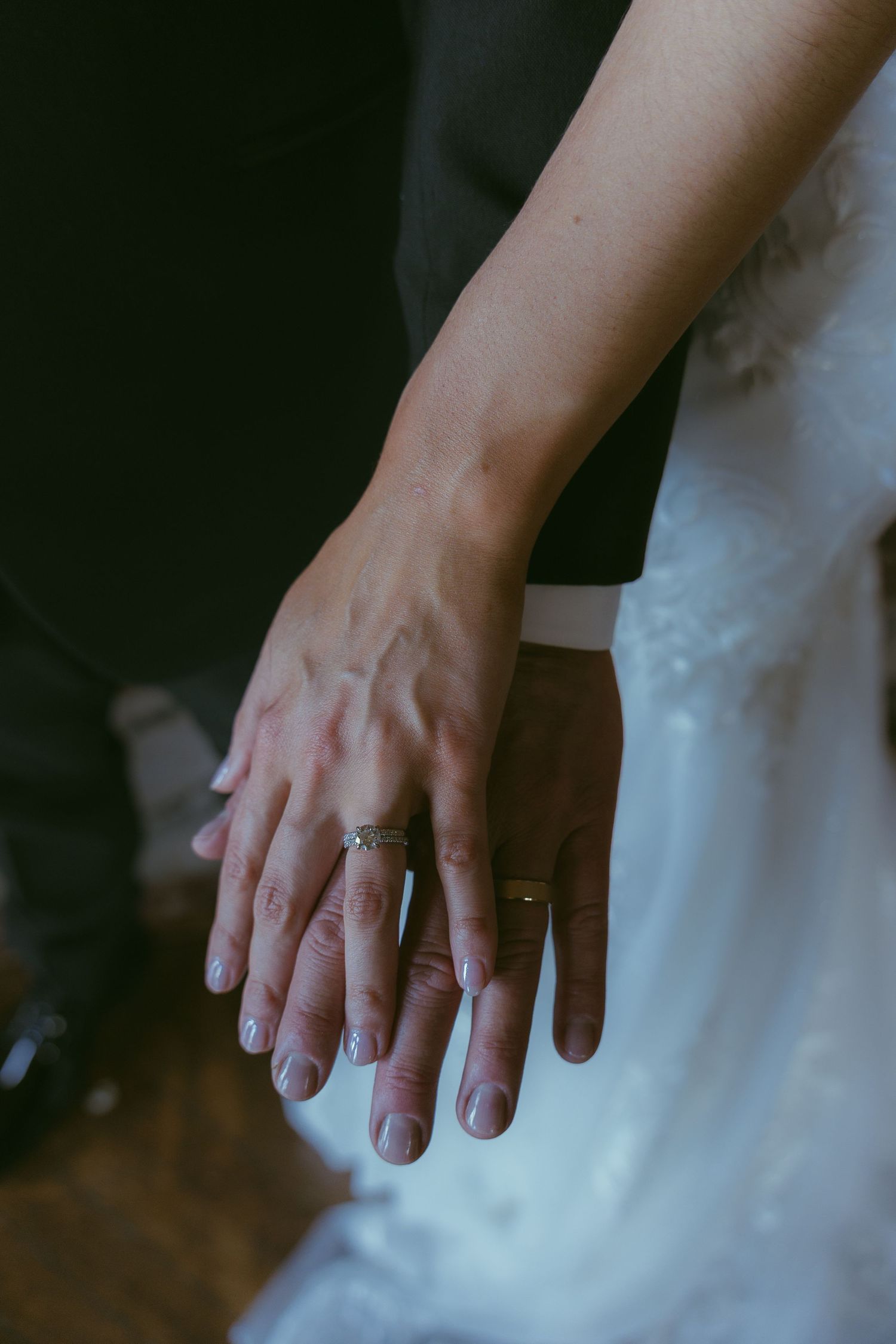 Close-up of hands wearing wedding rings against a white dress background.