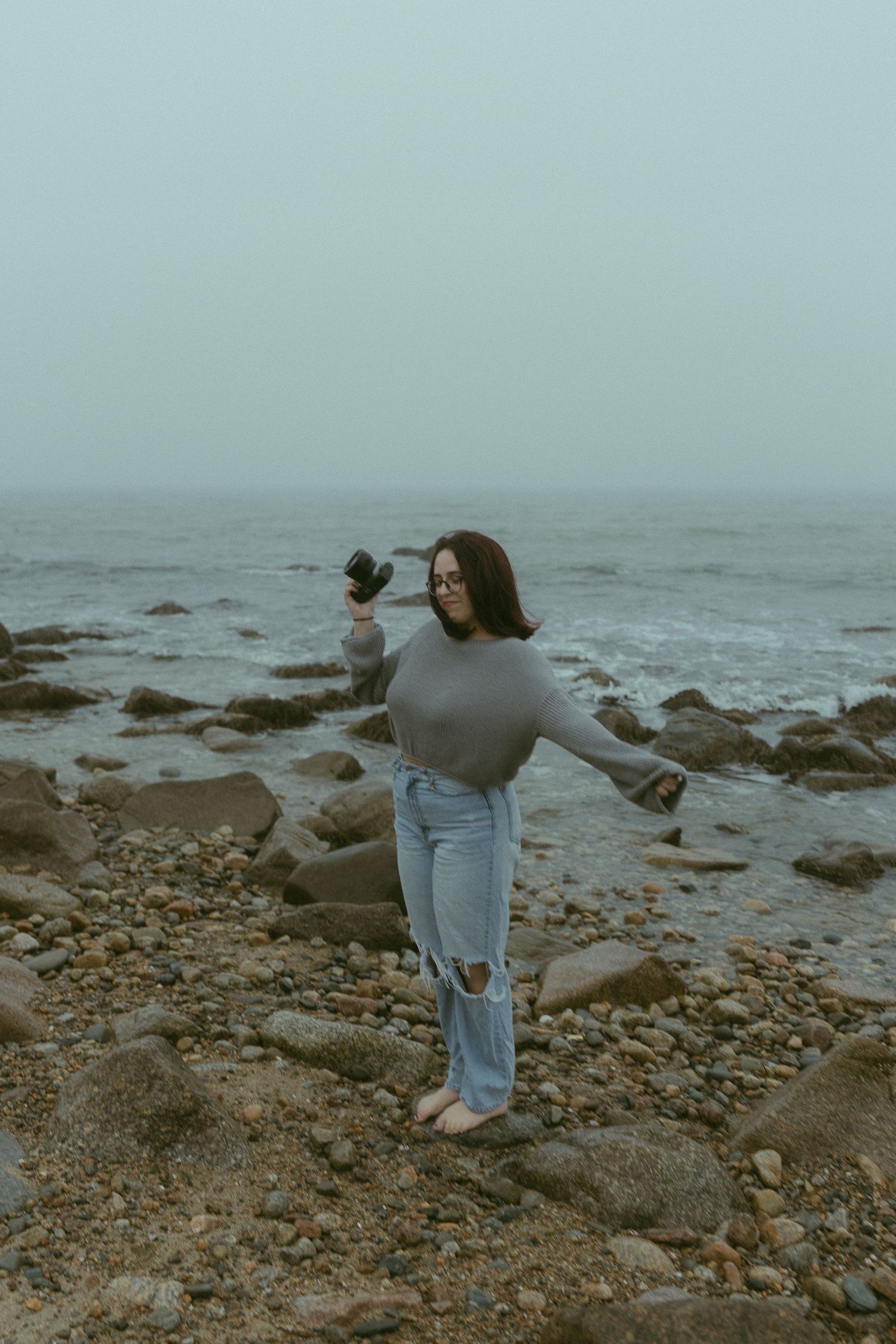 Two people exploring a rocky coastline on a misty overcast day.