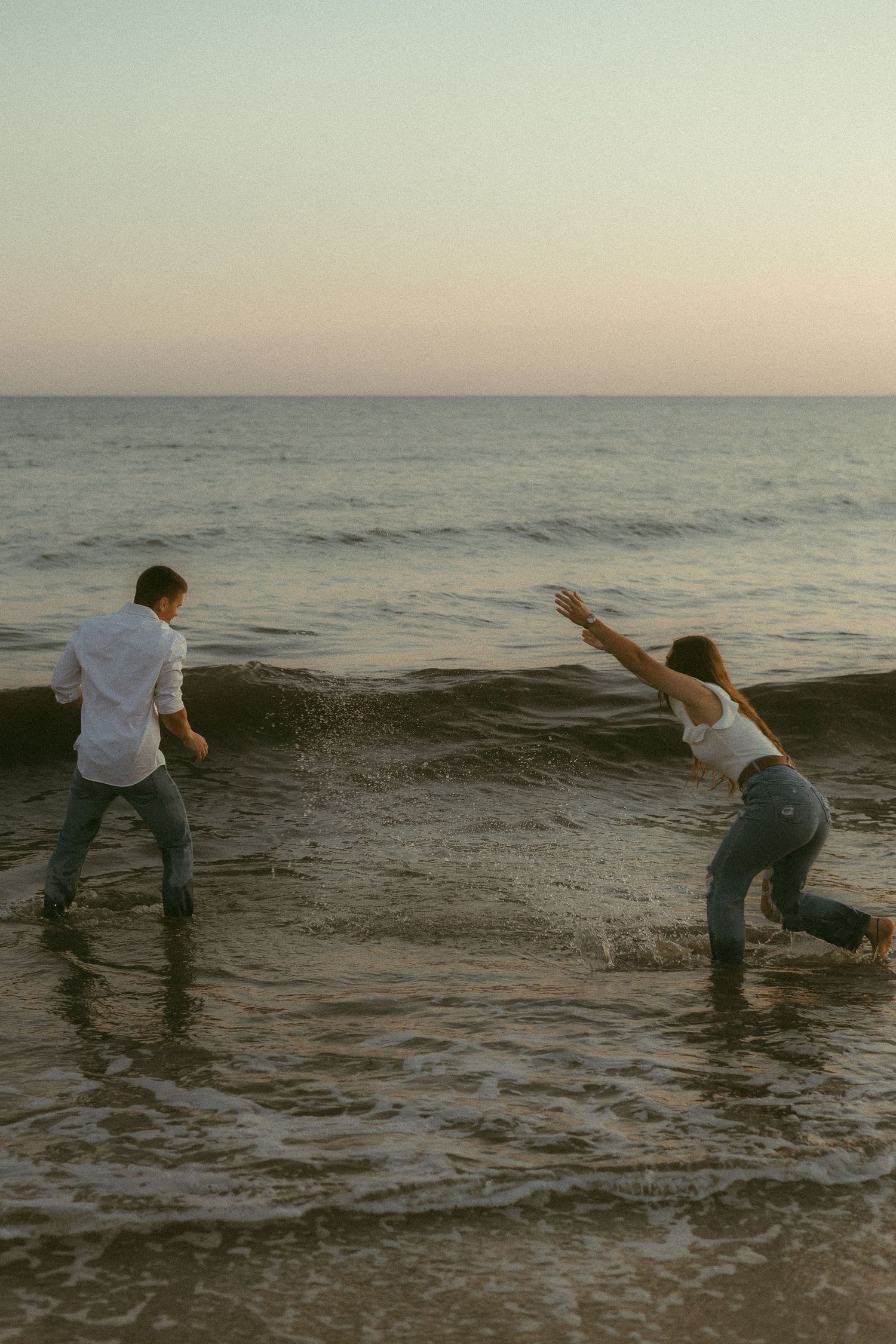 A playful couple splashing in ocean waves at sunset.