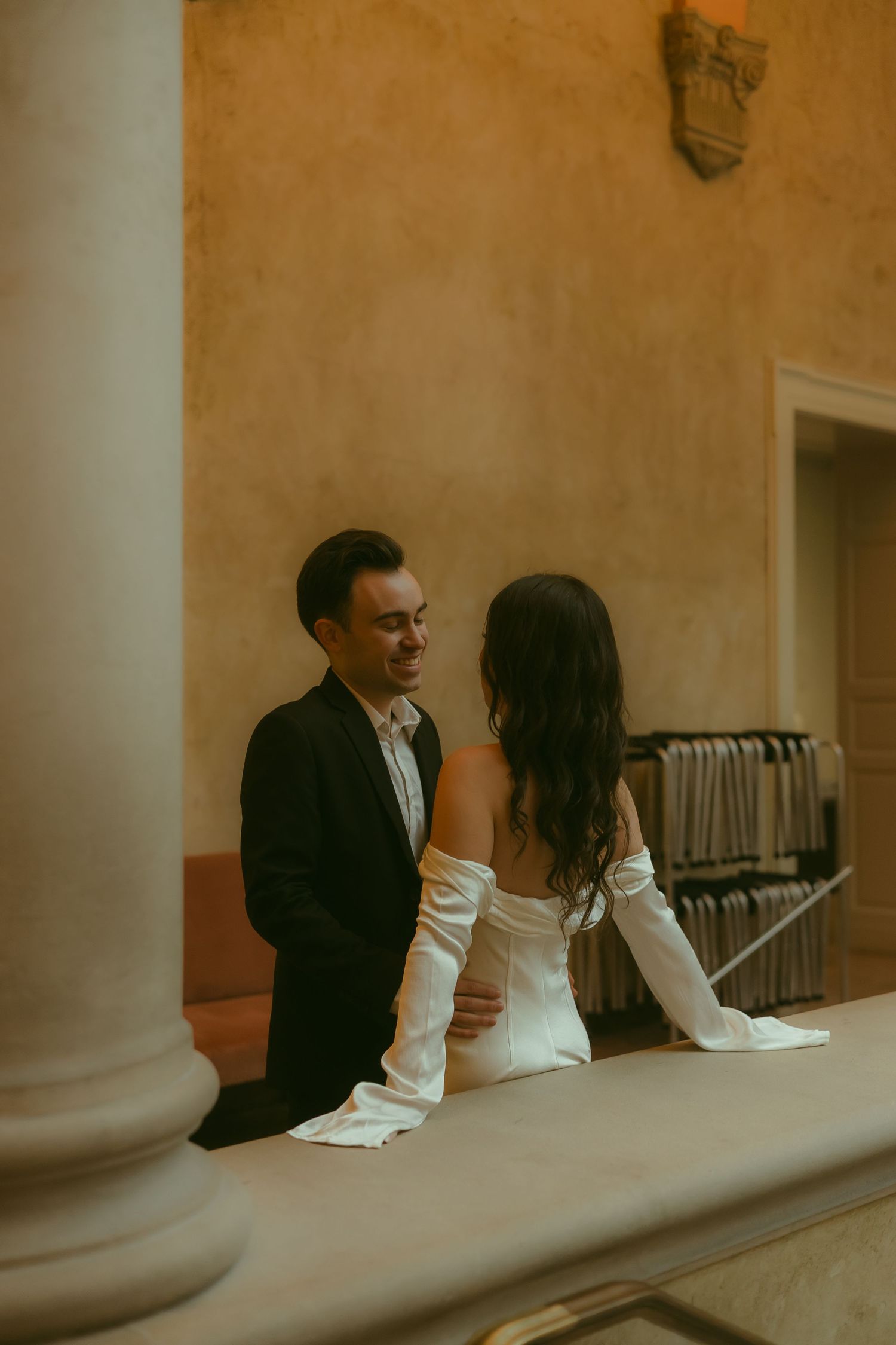 A couple shares an intimate moment against a warm-toned wall with white columns.