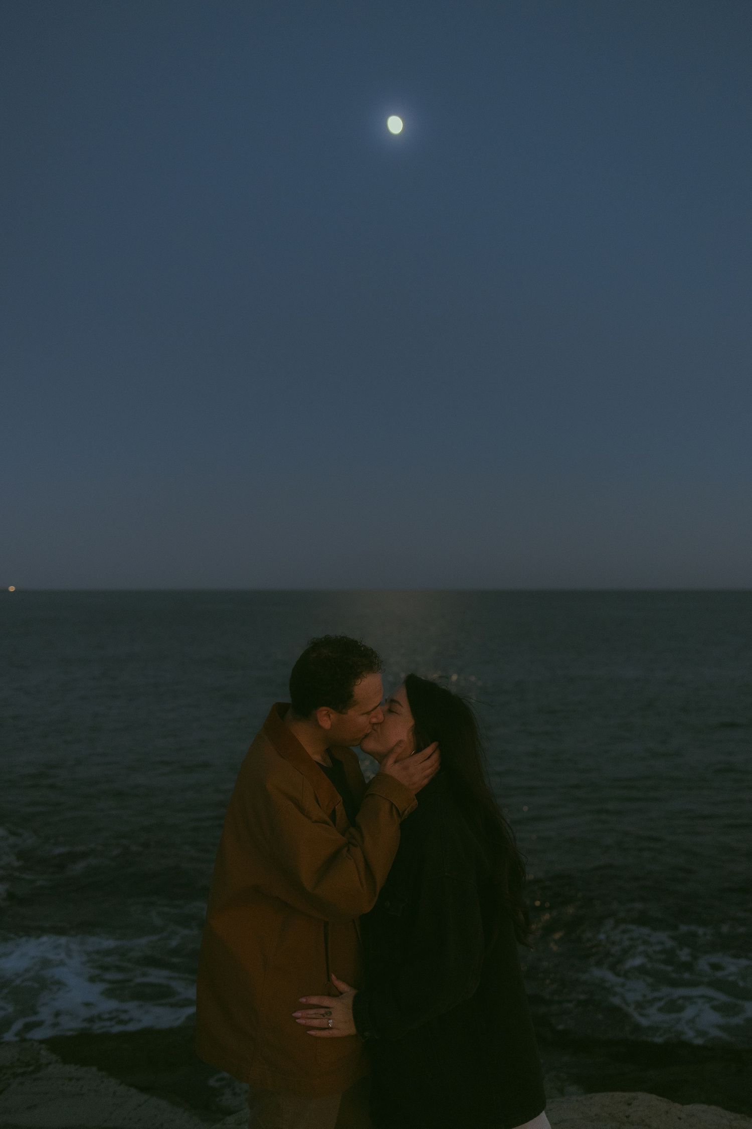 A romantic moonlit embrace by the ocean at night.