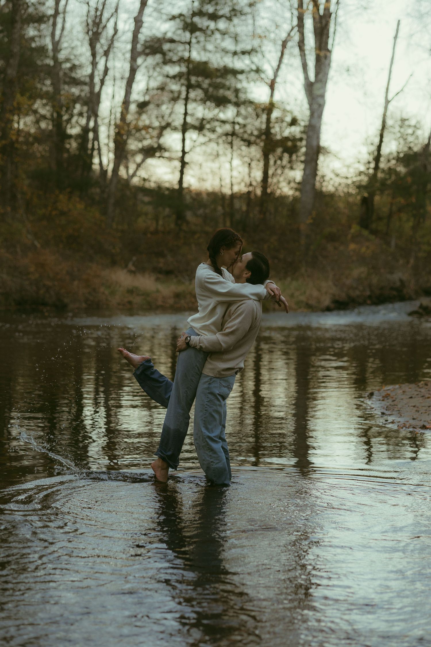 Silhouettes dancing in shallow water at dusk with trees in the background.