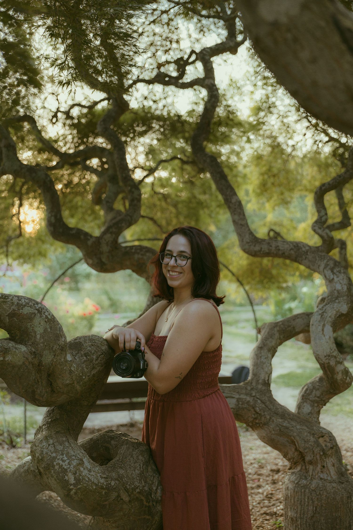 Person in burgundy dress posing joyfully under twisted oak tree branches.