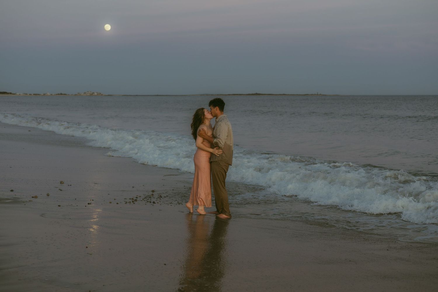 Couple sharing romantic moments on a misty beach at sunset.