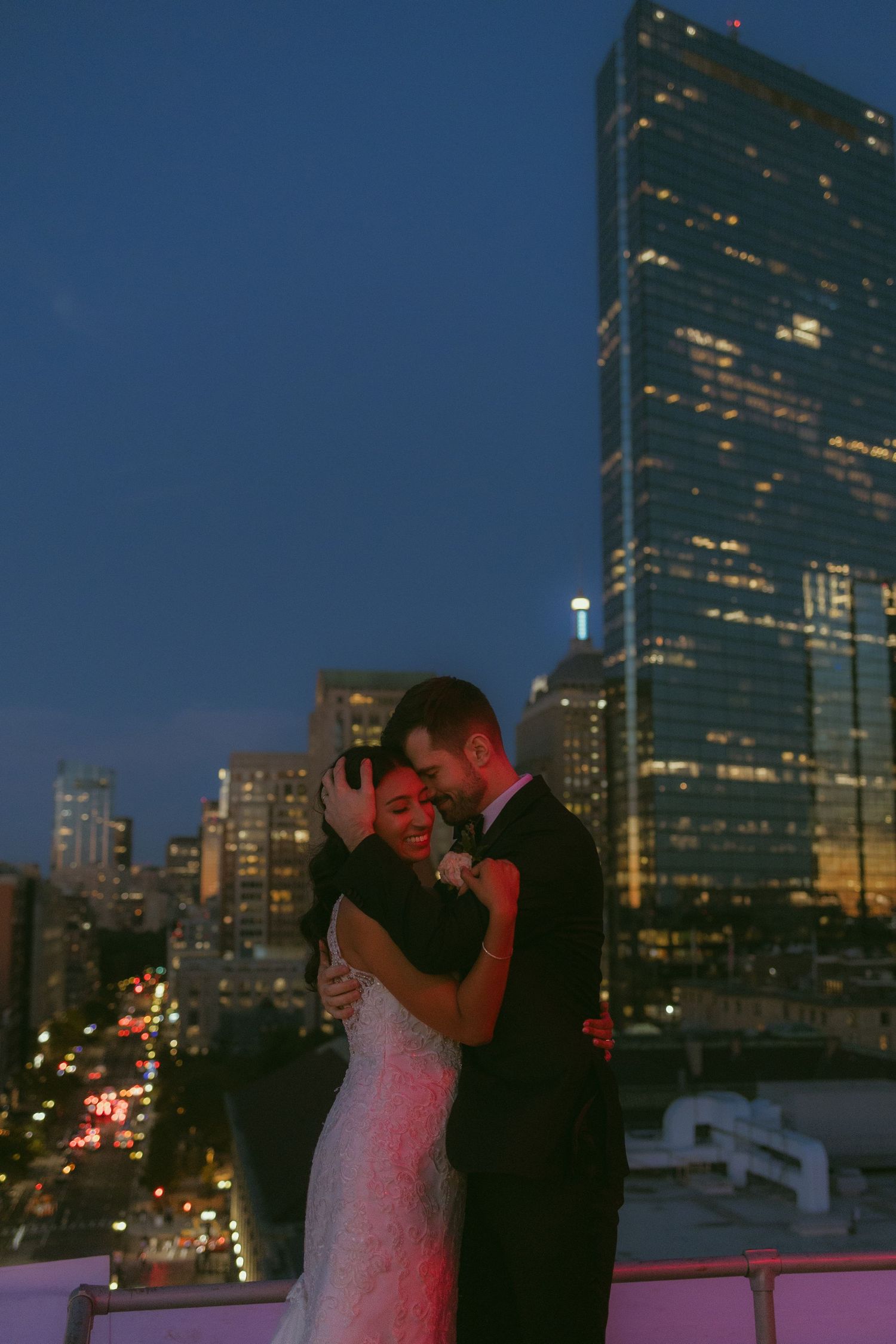 A nighttime wedding portrait with city lights and buildings in the background.