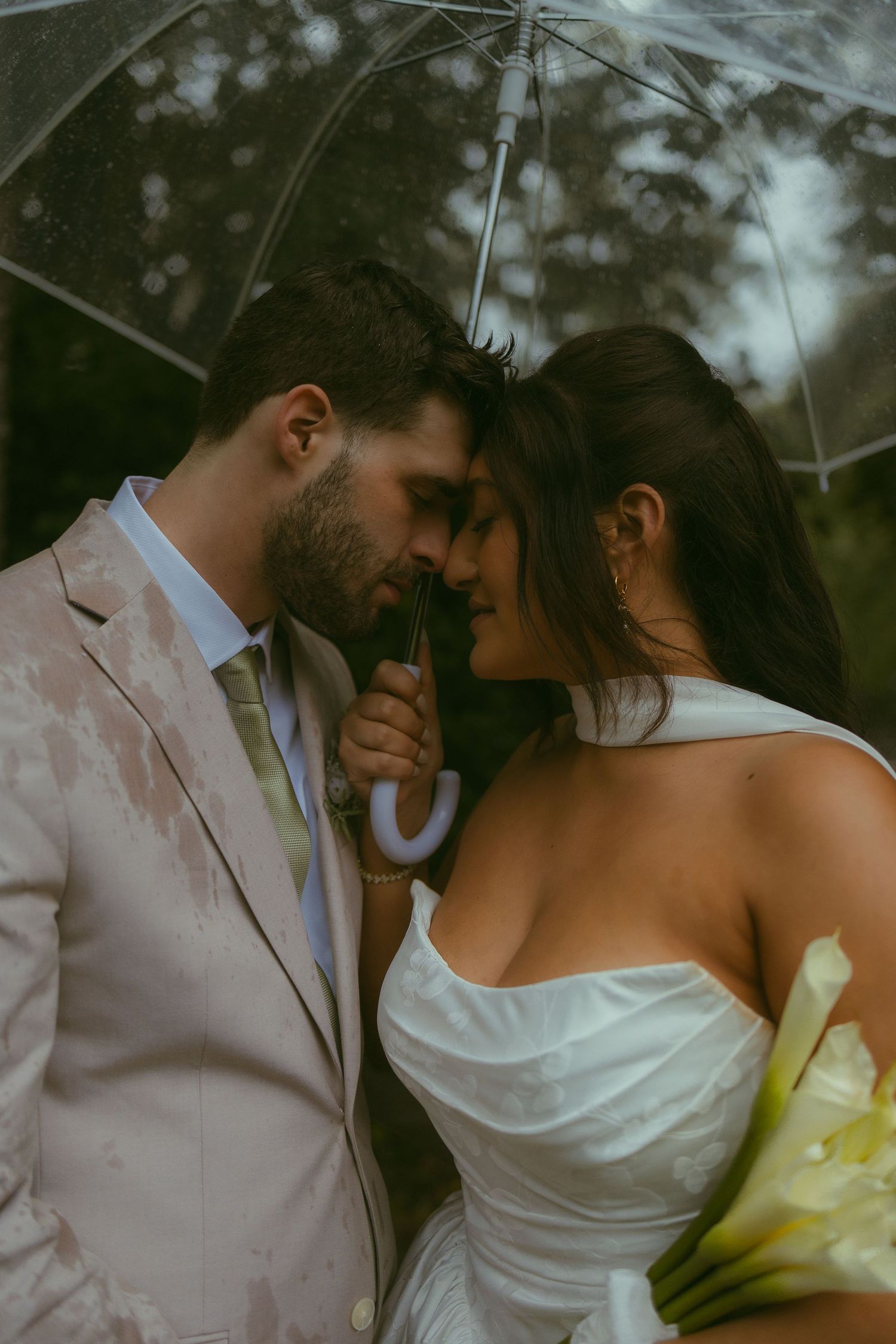A romantic moment shared under a clear umbrella in formal attire.
