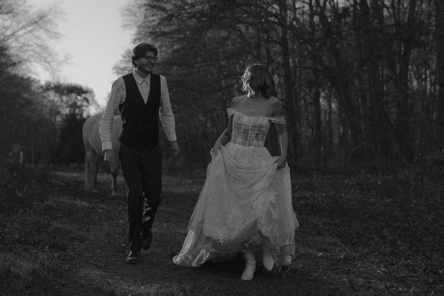 A couple walks through a misty forest path in black and white.