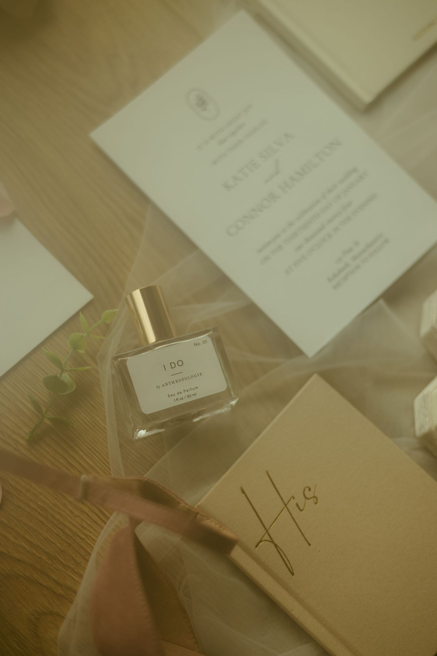 Wedding stationery and perfume bottle arranged on wooden surface in soft lighting.