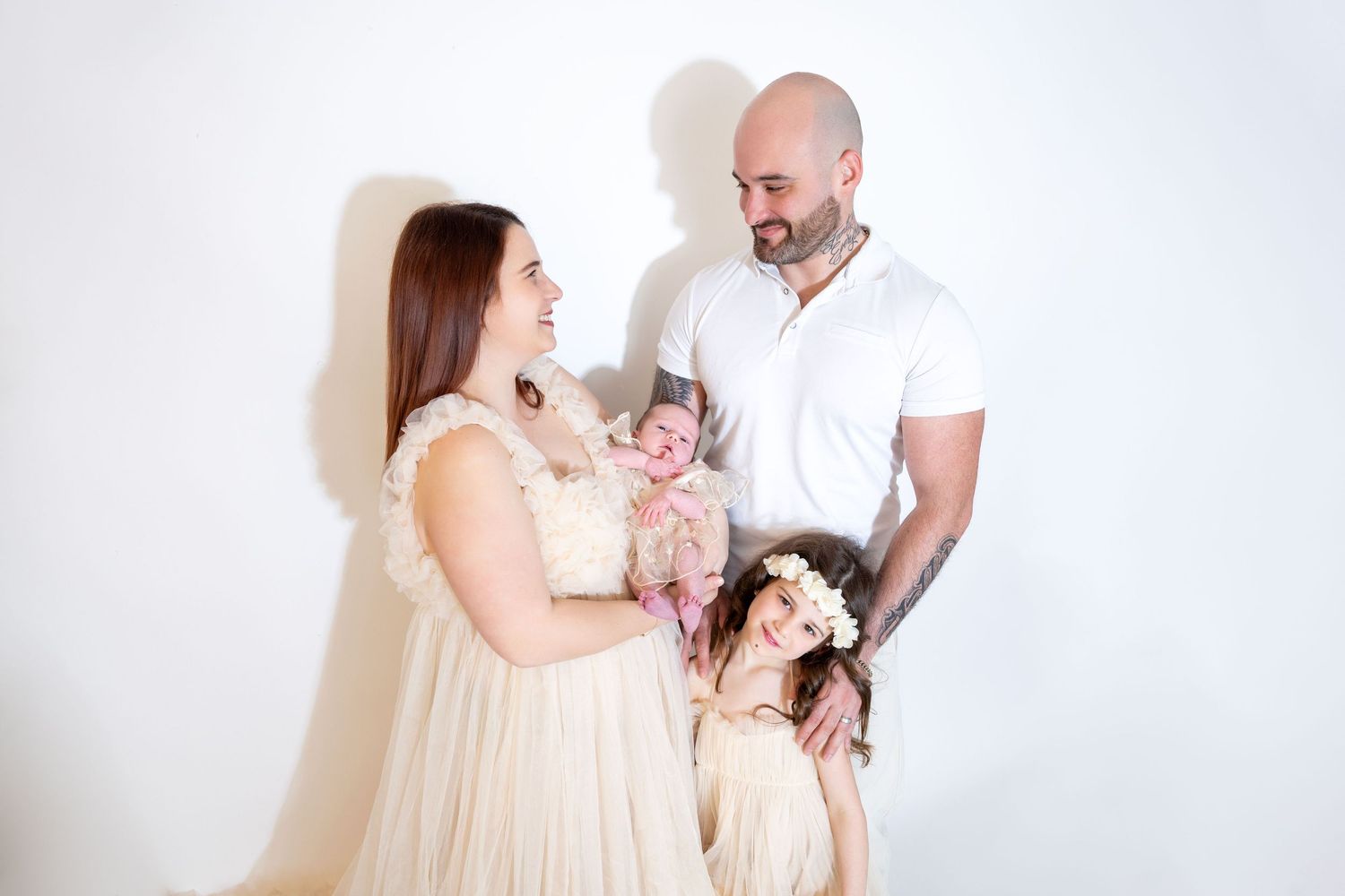 A family of four shares a tender moment with their newborn baby in a bright studio setting.