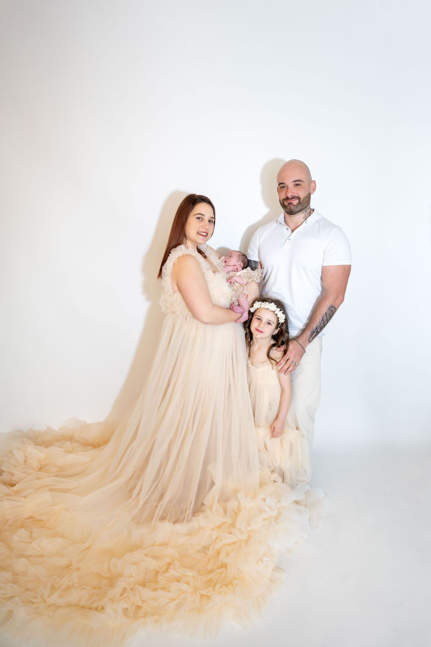 A family poses together with their newborn baby, older daughter in a floral crown, in a studio.