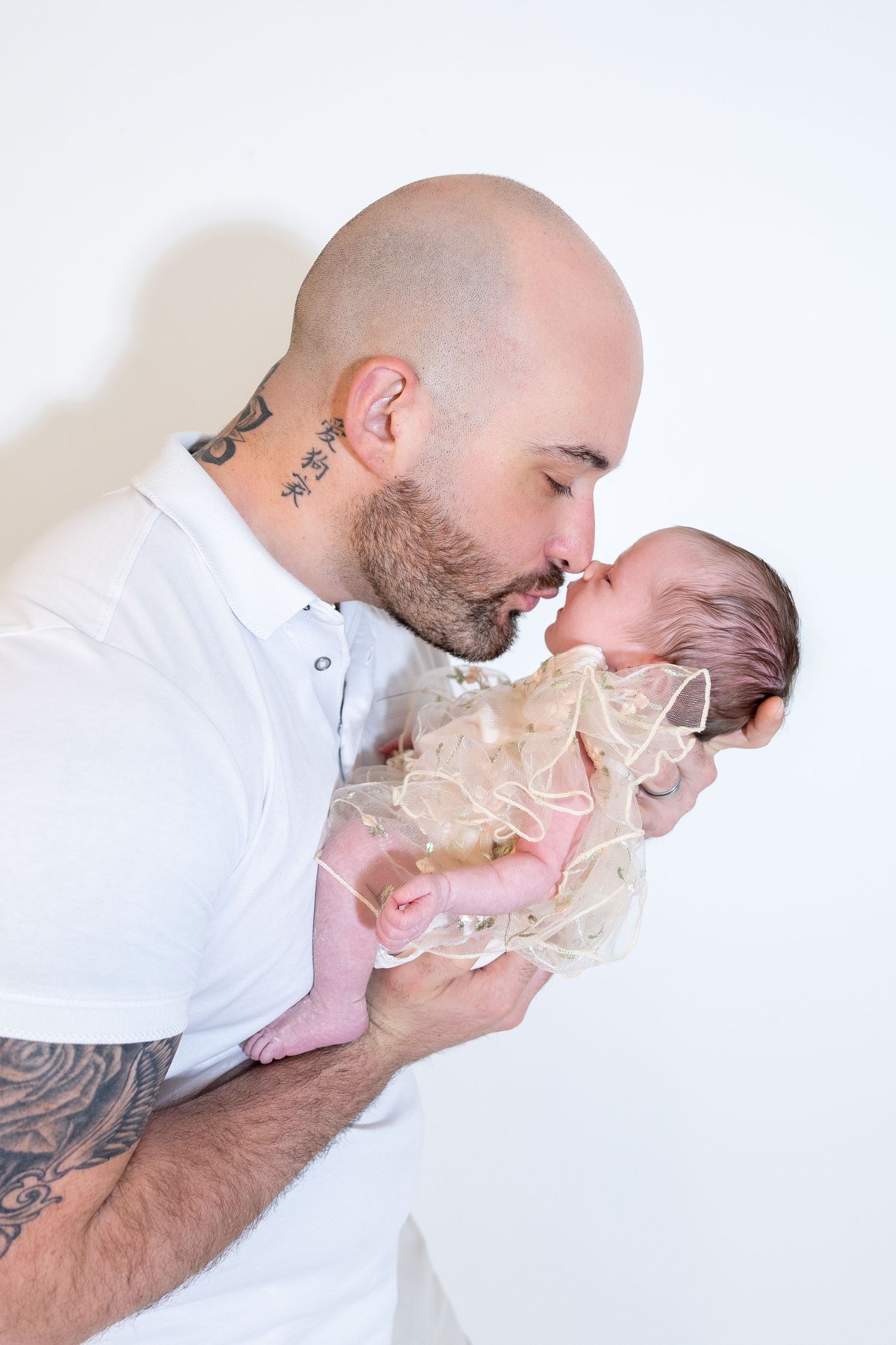 A tattooed father gently kisses his newborn baby in a heartwarming black and white studio photo.
