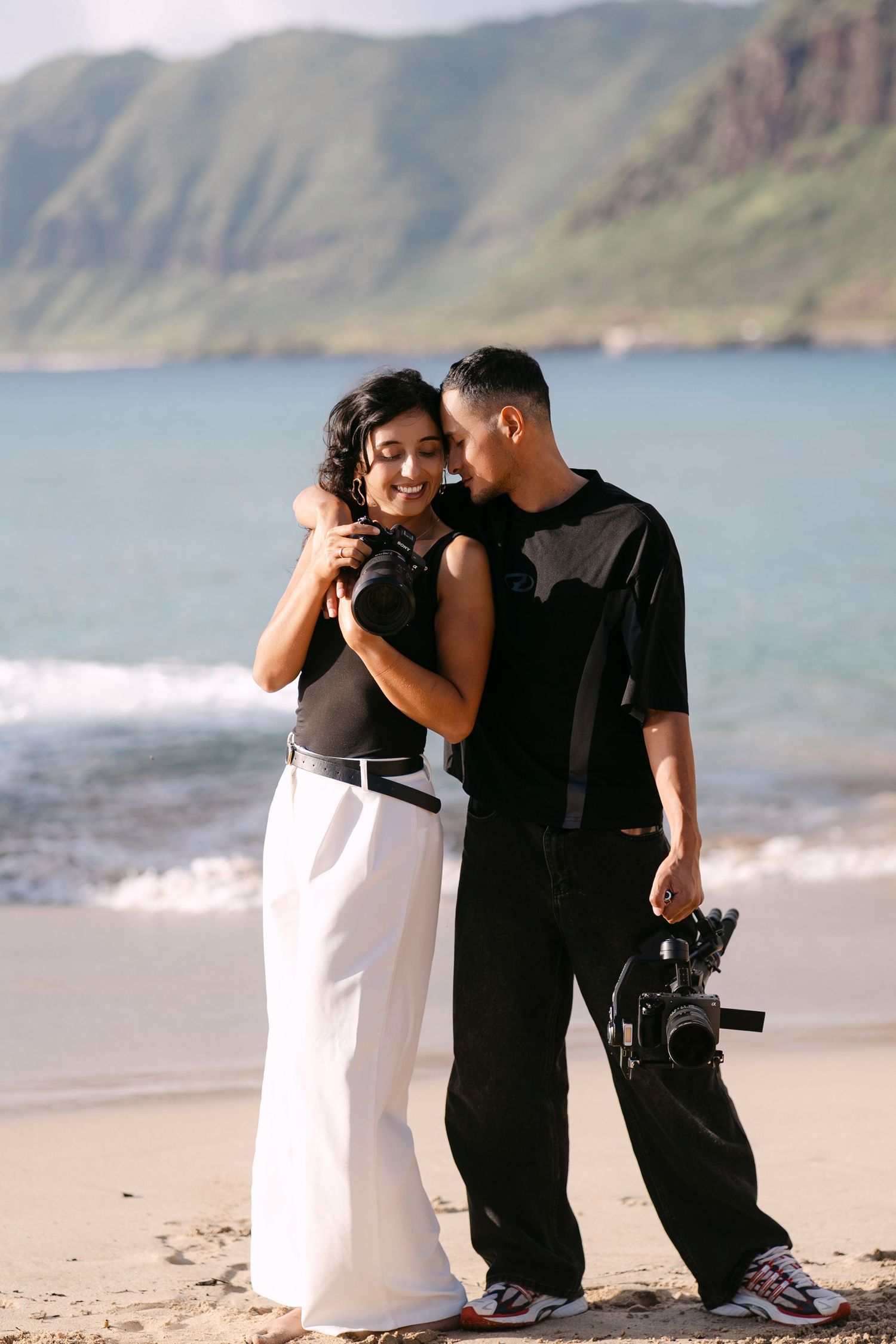 A couple shares romantic moments on a scenic beach with mountains in the background.