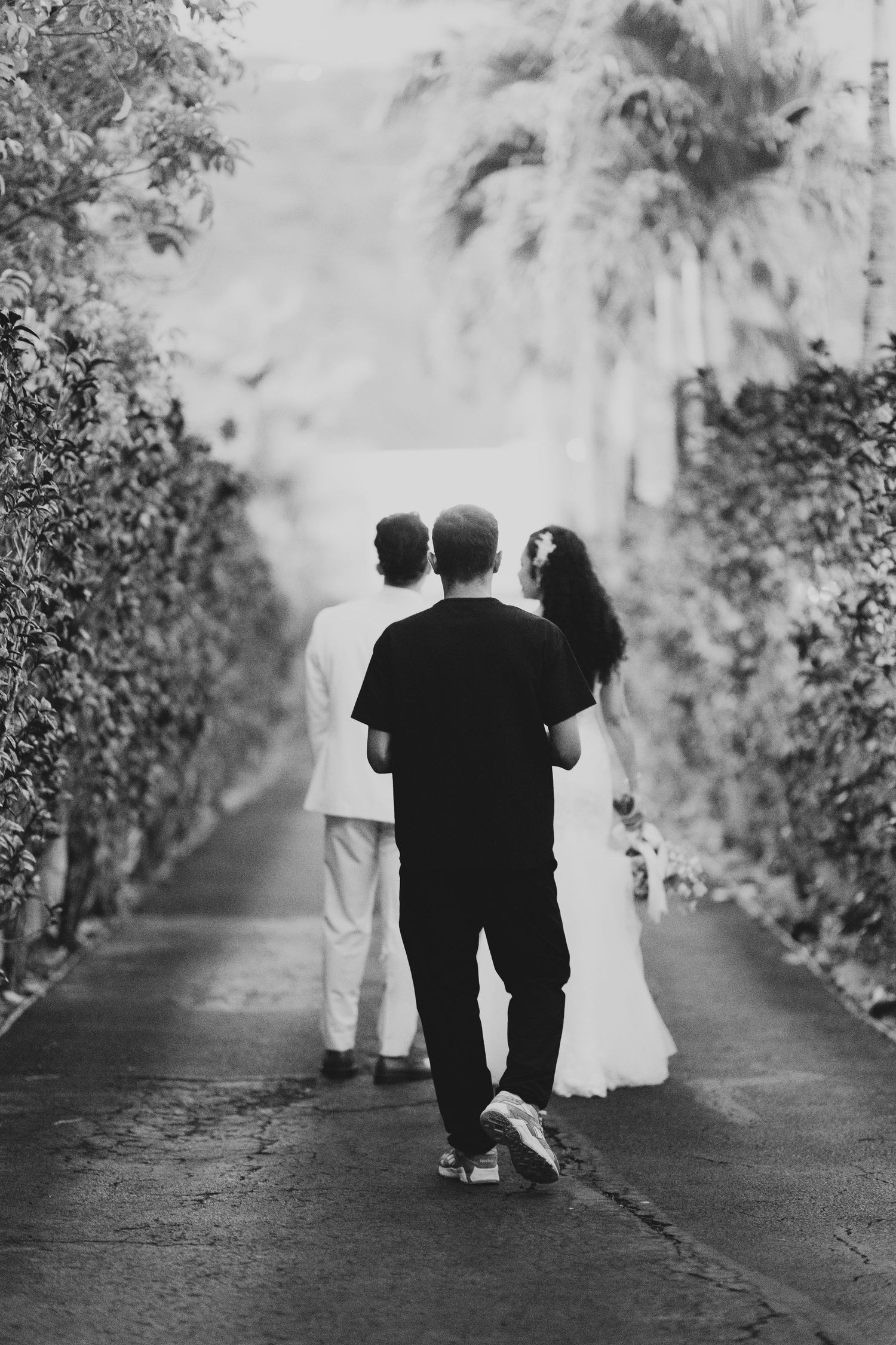 Black and white photo series showing three people walking away down a tree-lined path in a romantic garden setting.