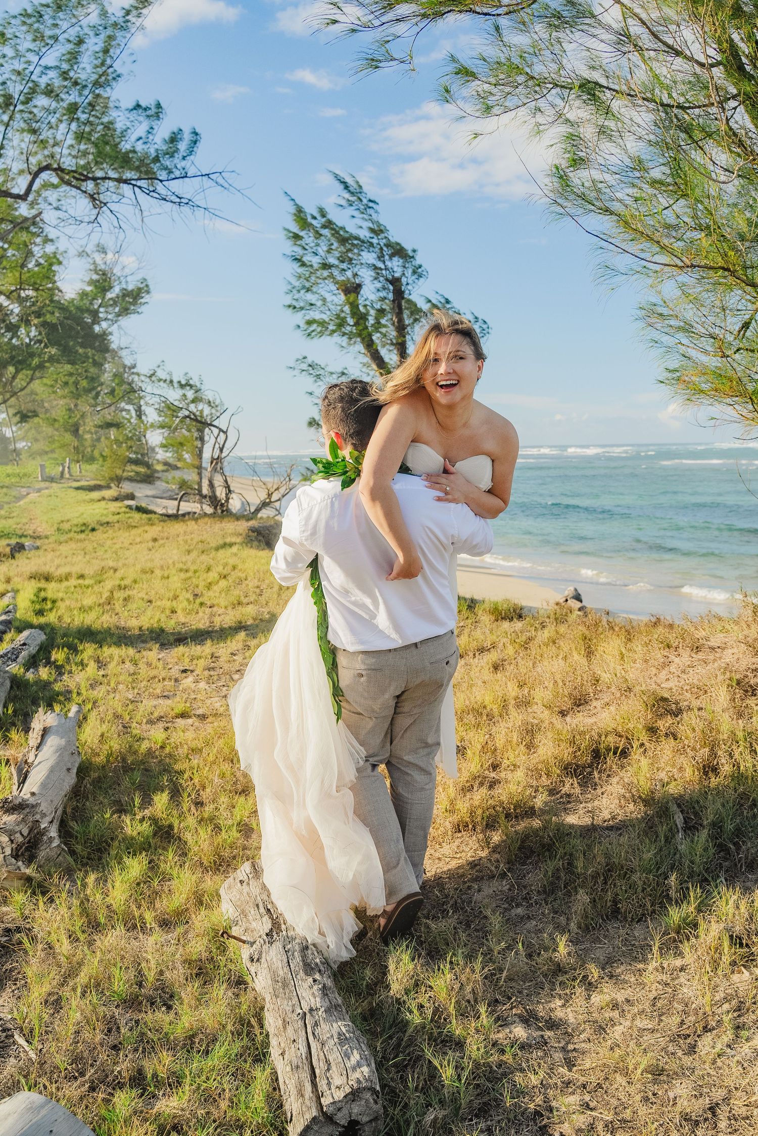 A joyful couple share a romantic moment on a coastal cliffside path with ocean waves and blue skies in the background.