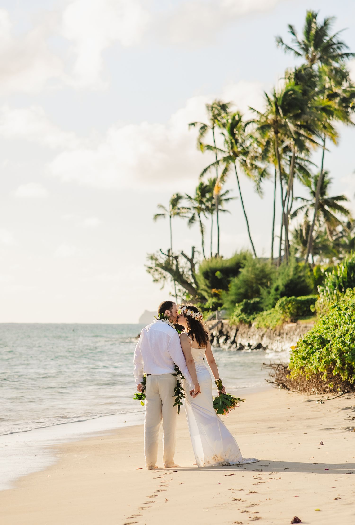 A couple strolls hand in hand along a tropical beach with swaying palm trees and golden sand at sunset.
