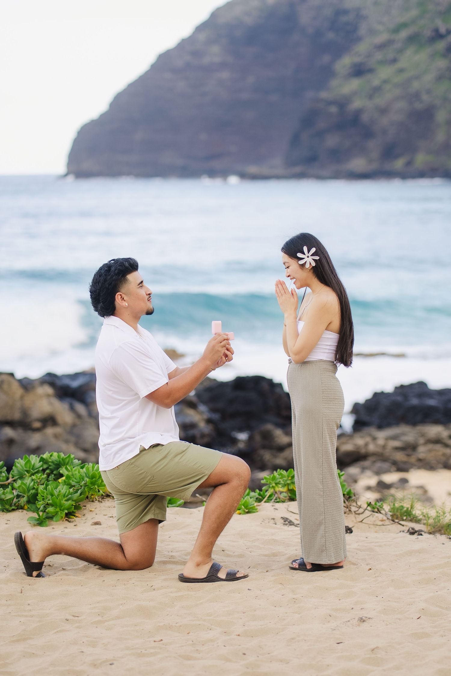 A proposal sequence showing a couple on a beach with ocean and cliffs in the background during a surprise moment.