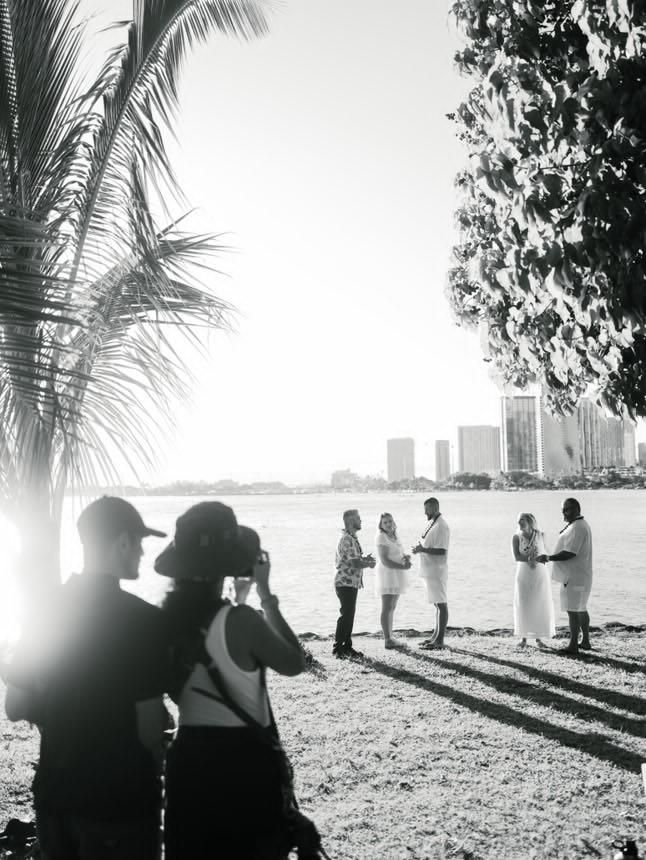 Silhouettes of people gathered on a beach at sunset with palm trees casting long shadows on the sand.