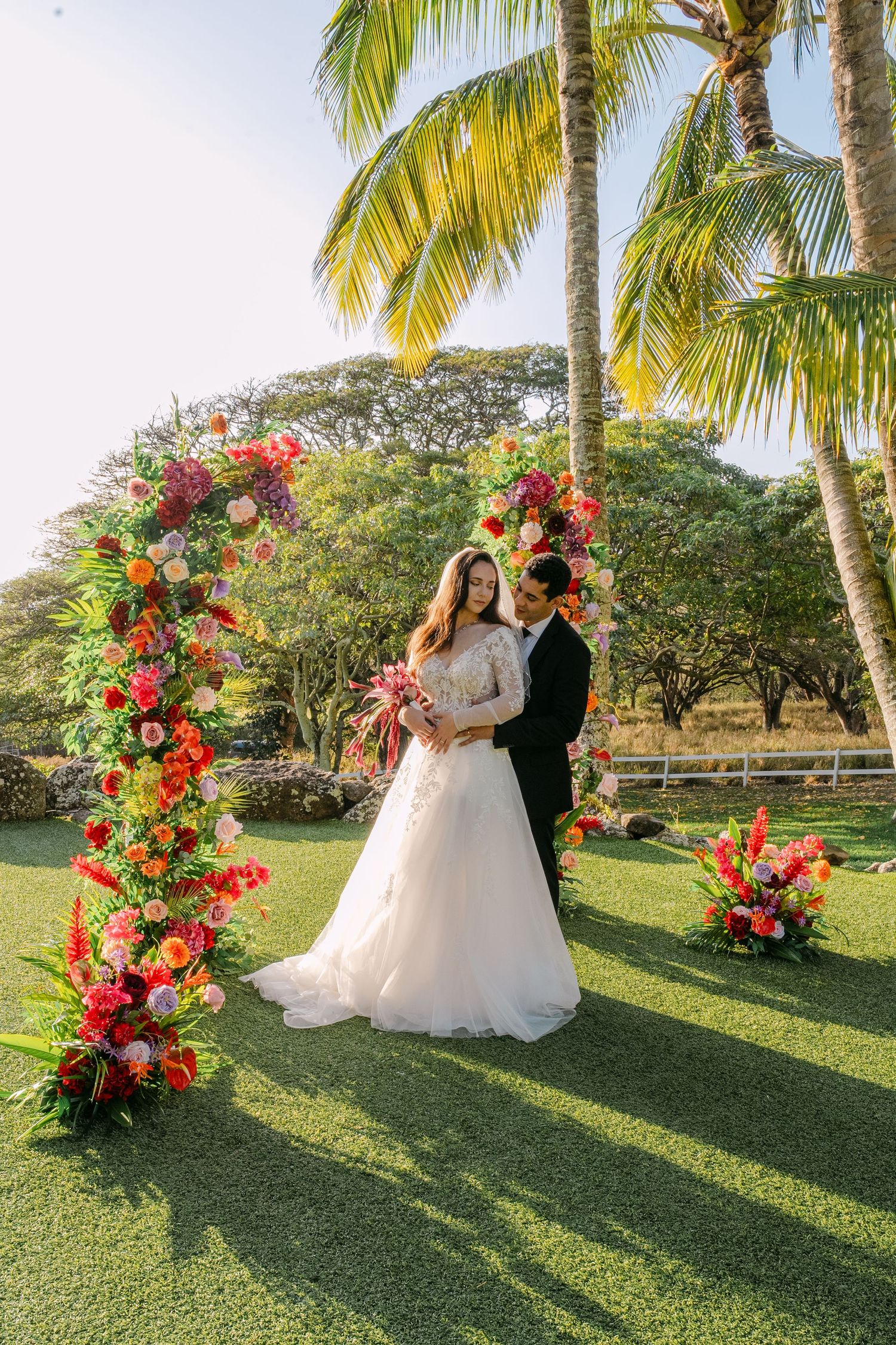 Couple shares romantic moments in a tropical garden setting with vibrant coral and orange floral arrangements and palm trees.