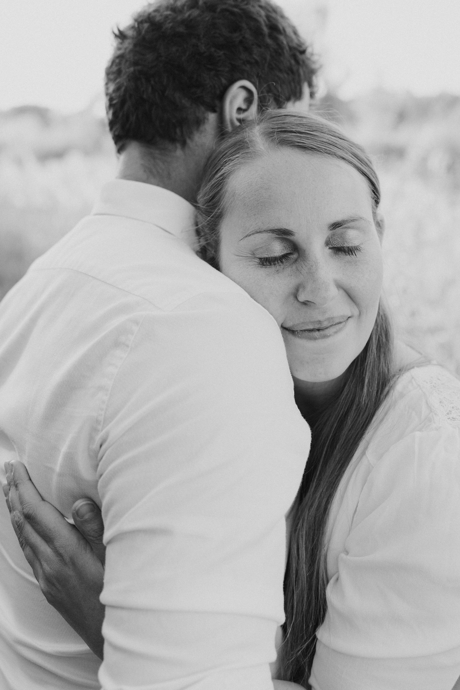 Frau lehnt sich entspannt an ihren Partner und lächelt. Ruhiges und emotionales Paarfoto