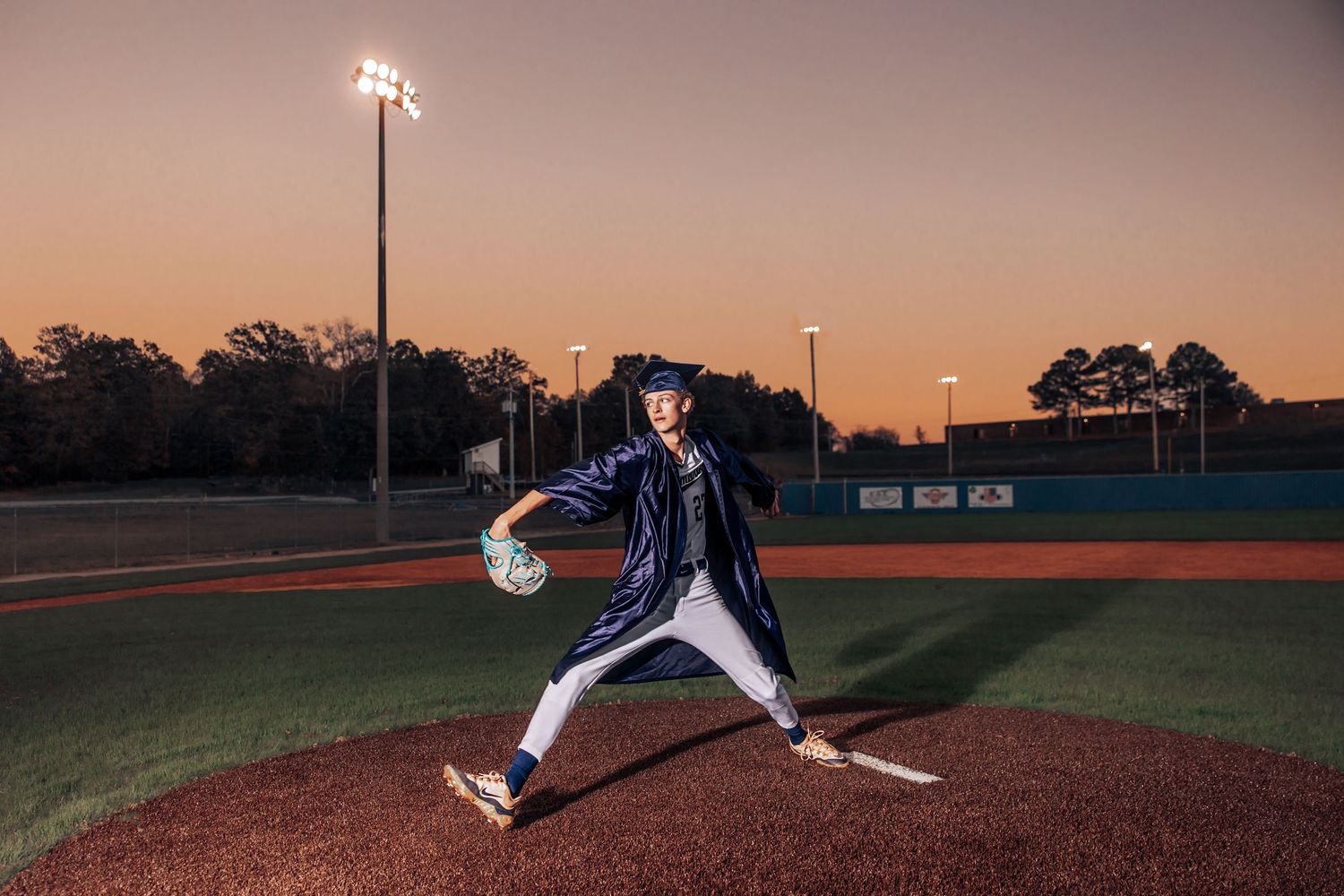 Baseball pitcher in mid-throw motion on pitching mound at dusk with stadium lights illuminating the field.