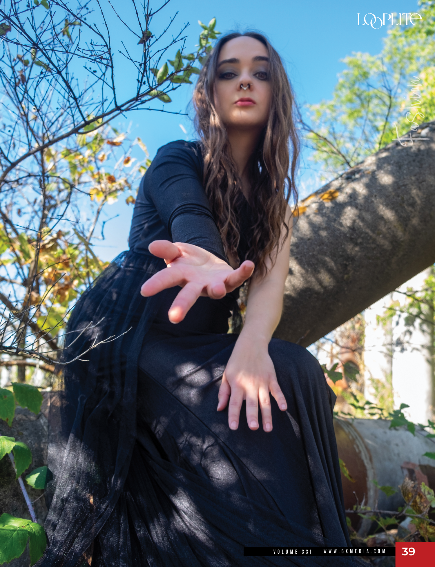 Gothic-styled outdoor fashion portrait with dappled sunlight and reaching gesture.