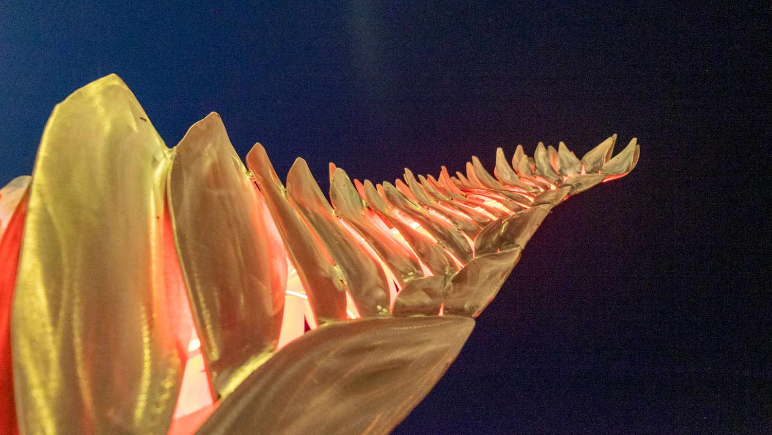 Close-up of a colorful glass sculpture with yellow, pink, and gold spiky ridges against a dark blue background.