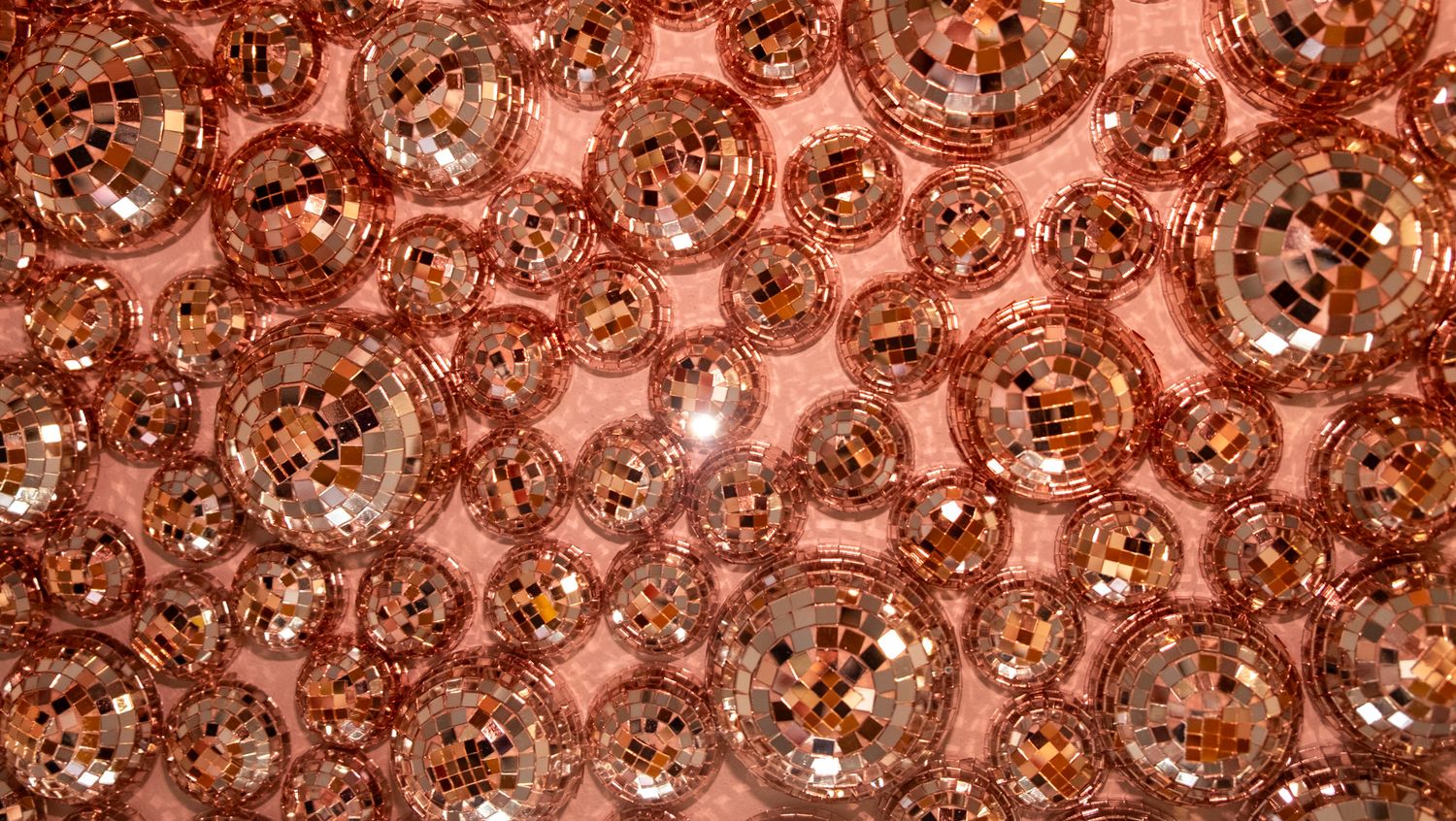 Rose gold mirror disco balls clustered together reflecting warm copper light on a pink background.