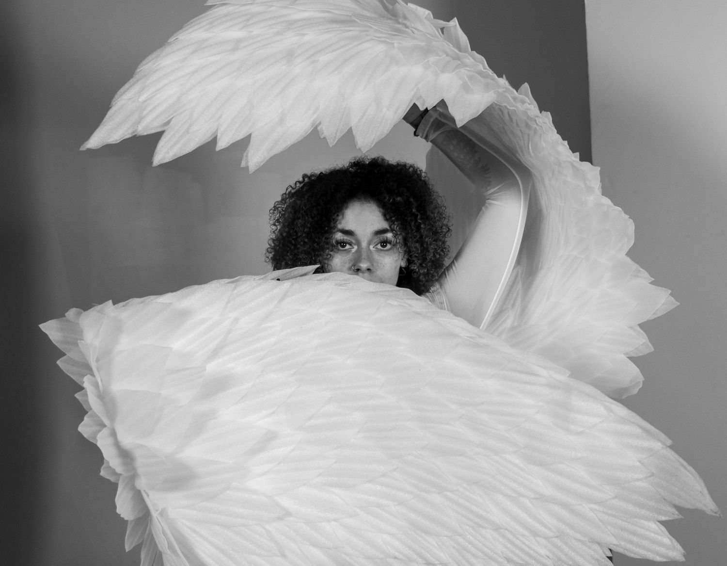 A series of black and white photographs showing someone wearing dramatic white feathered angel wings against dark backgrounds.