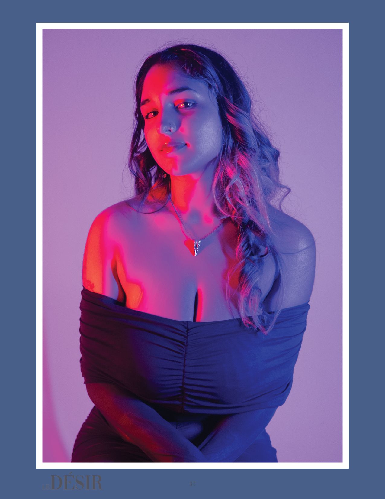 Model in dark dress poses against purple backdrop with dramatic red and blue lighting effects.