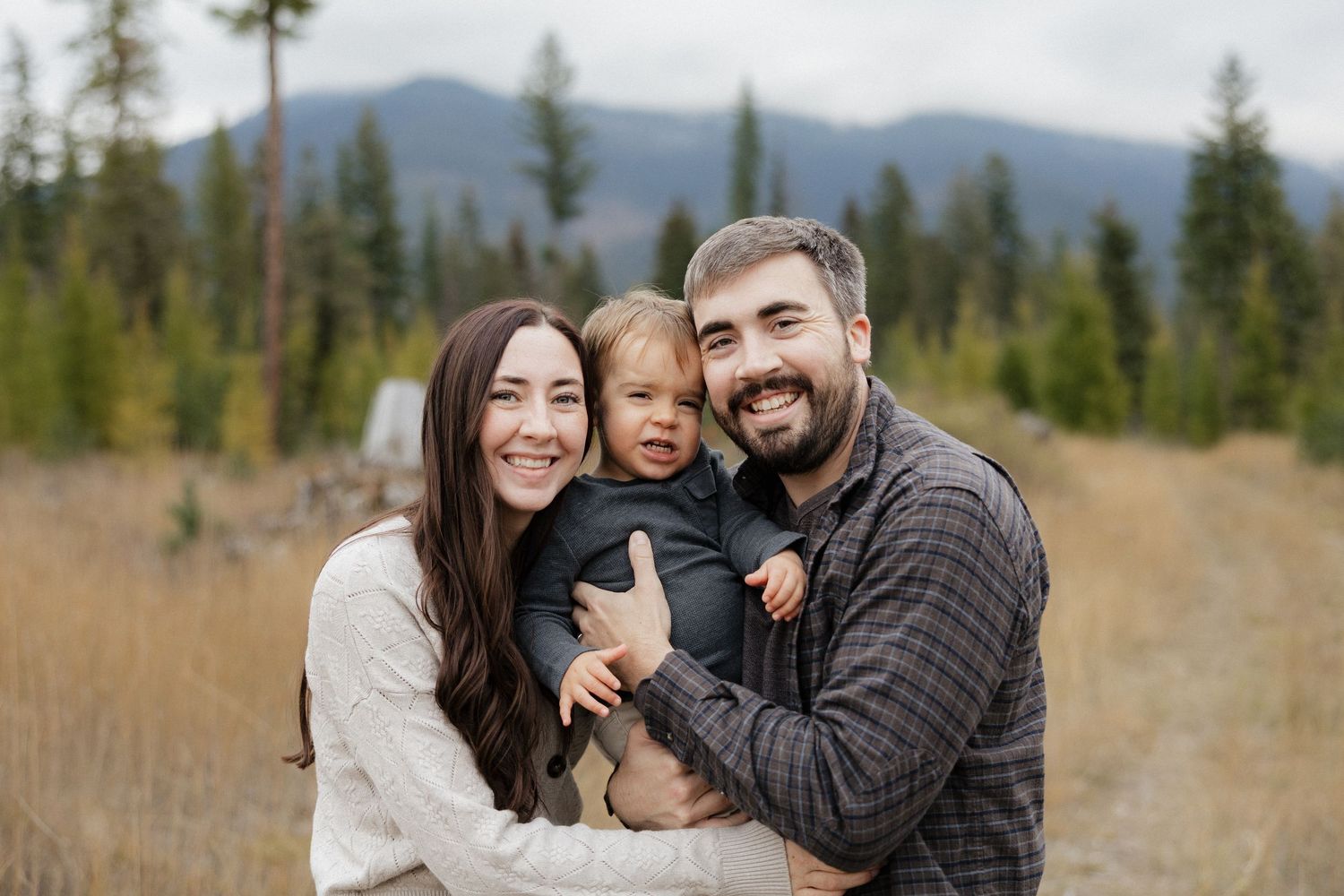A family shares joyful moments together in a scenic mountain field with evergreen trees in the background.