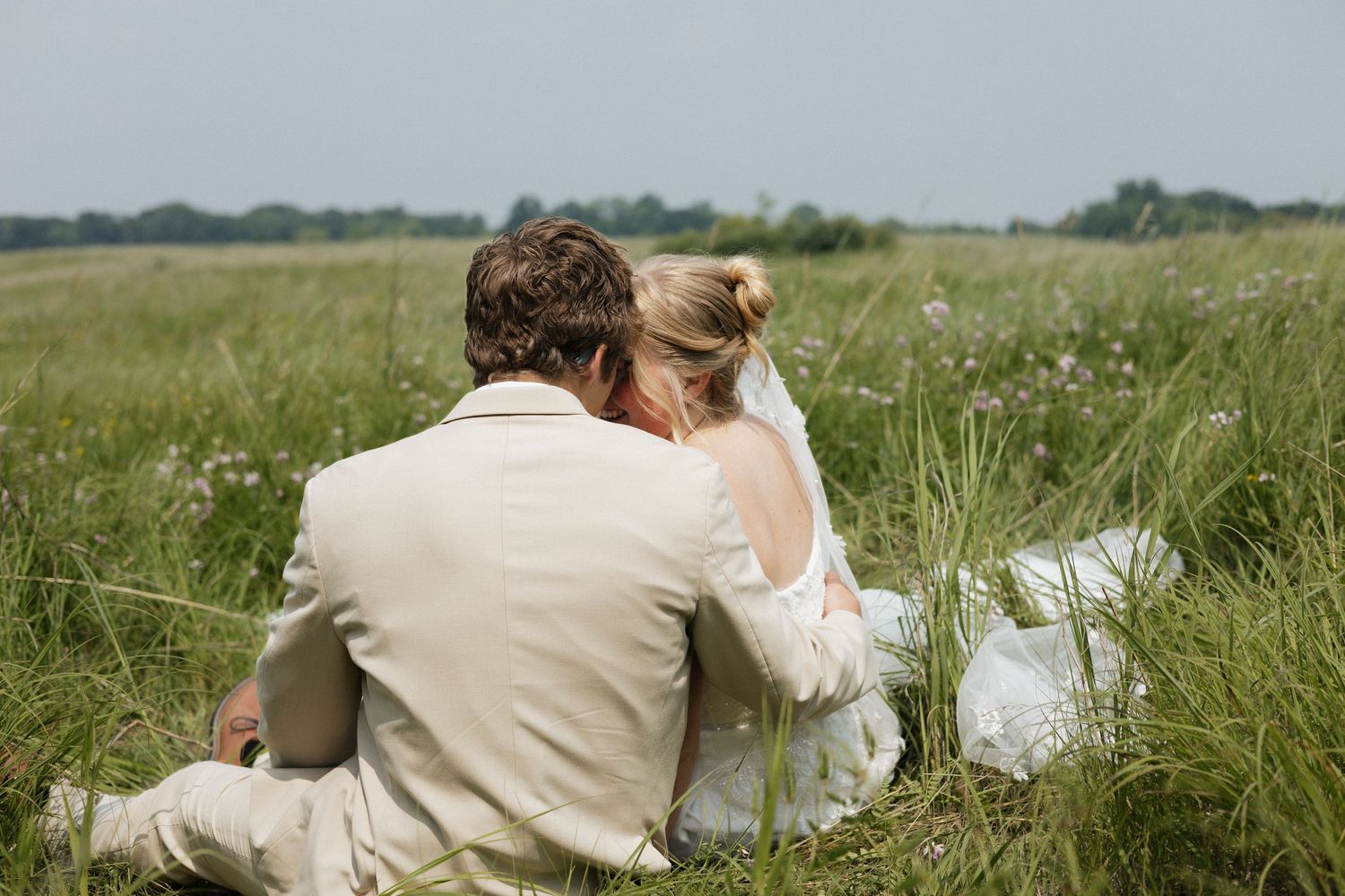 A person wearing a beige outfit lies in a serene green meadow on a sunny summer day.