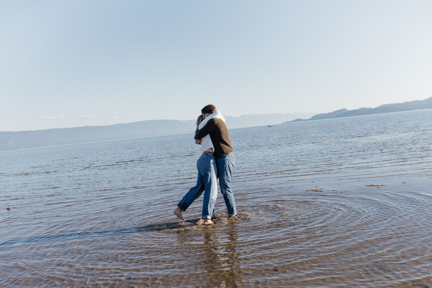 A person creates ripples in shallow coastal waters while walking along the shoreline at sunset.