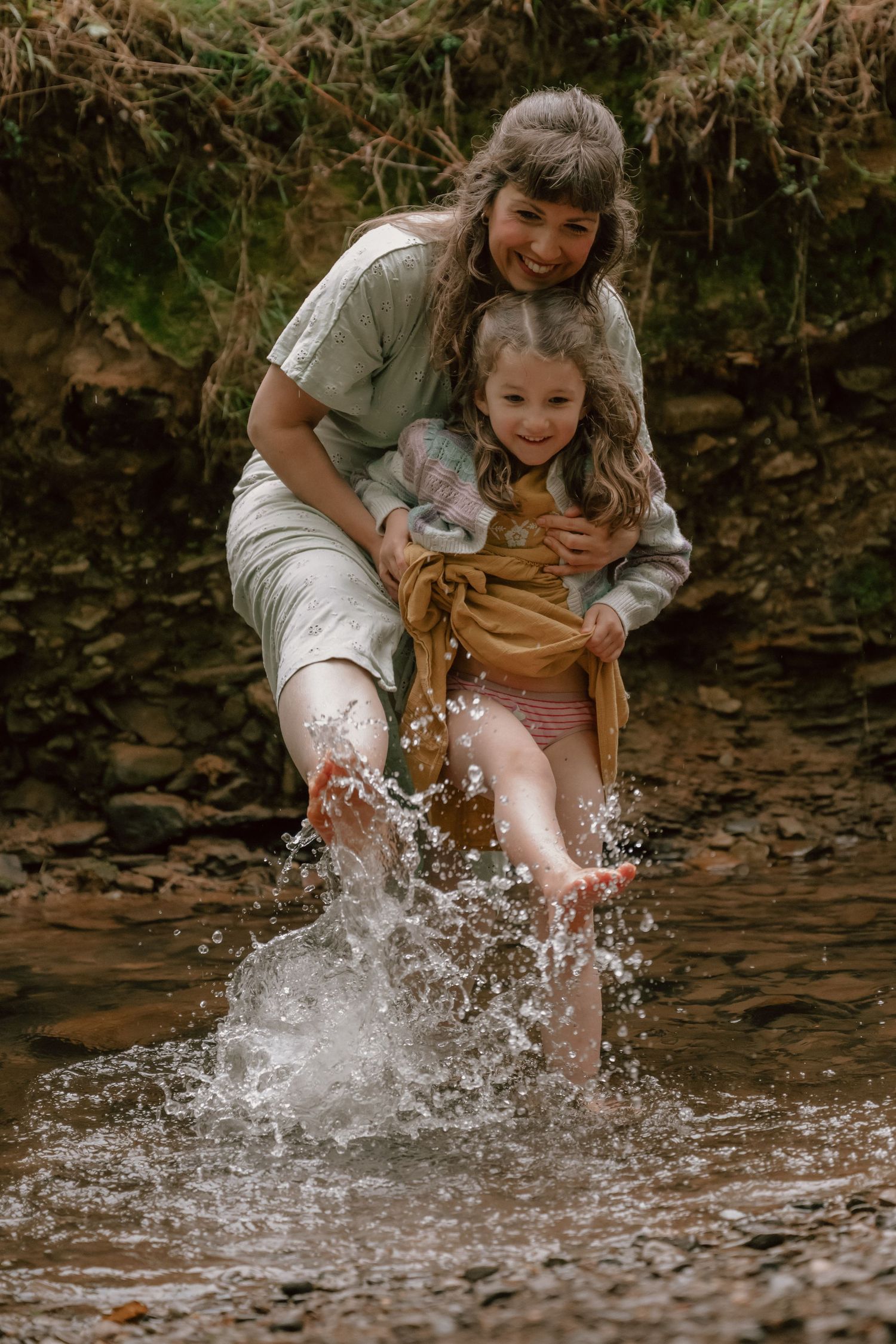 Playing and splashing in shallow creek water creates dynamic water droplets in motion against earthy rocky backdrop.