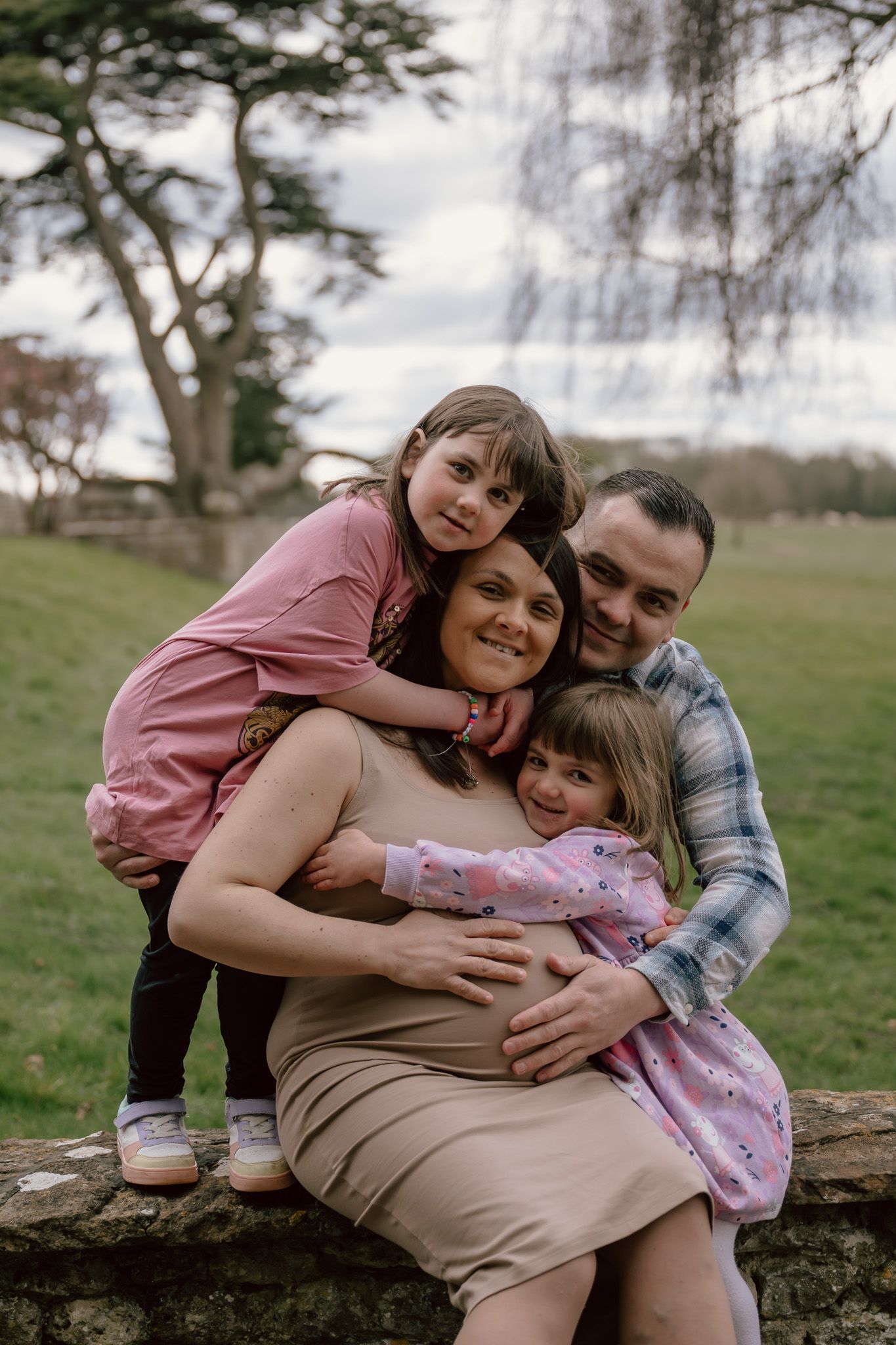 Family sharing tender moments while sitting on a stone wall in a pastoral outdoor setting.