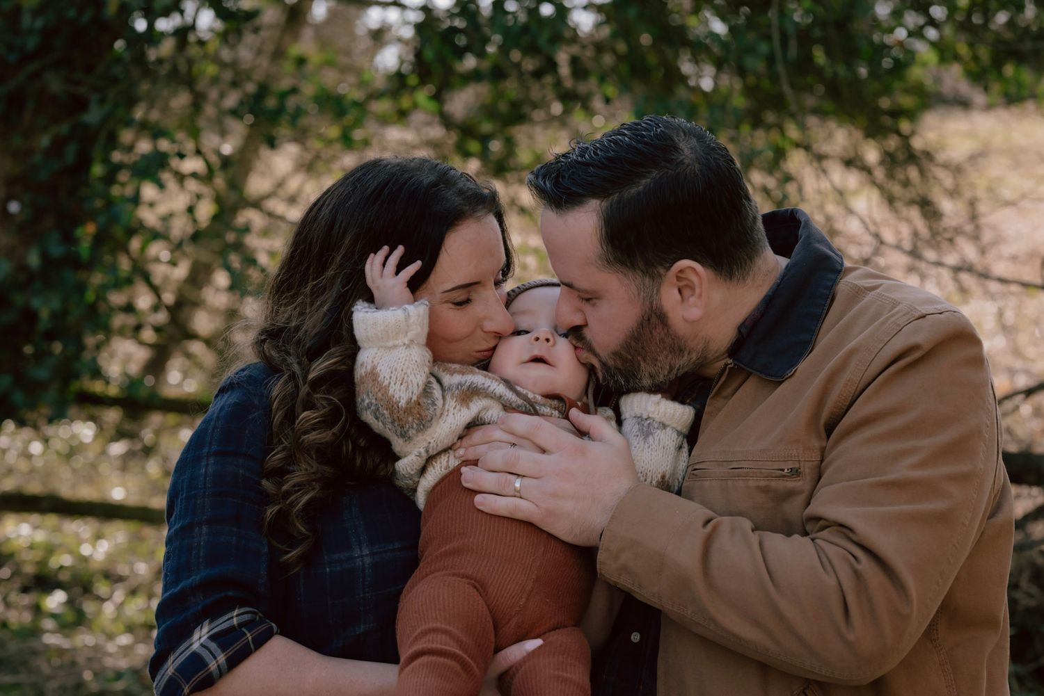 Loving parents share a tender moment outdoors with their baby in warm autumn clothing.