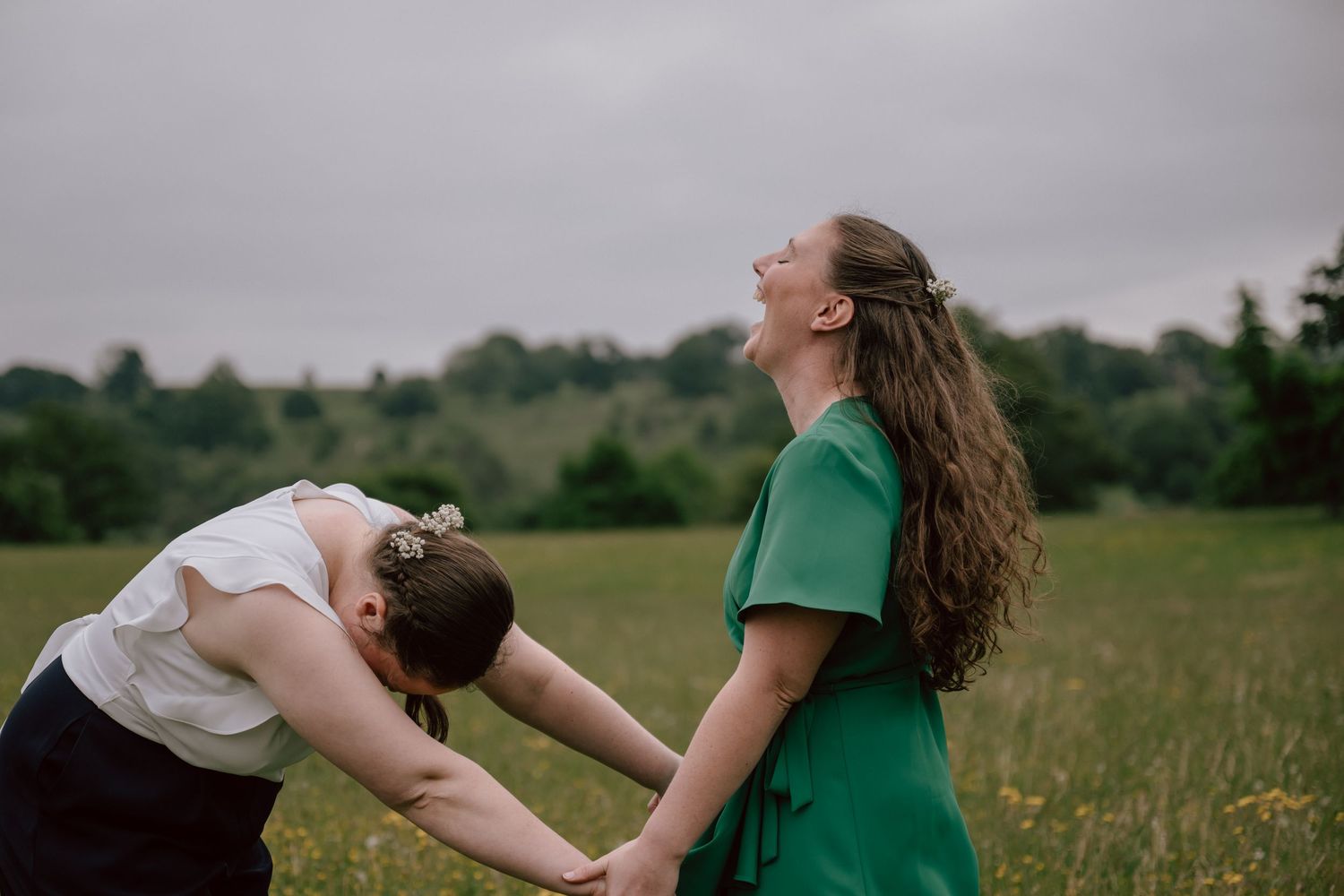 Two people in a field bend backwards in playful poses against an overcast sky background.