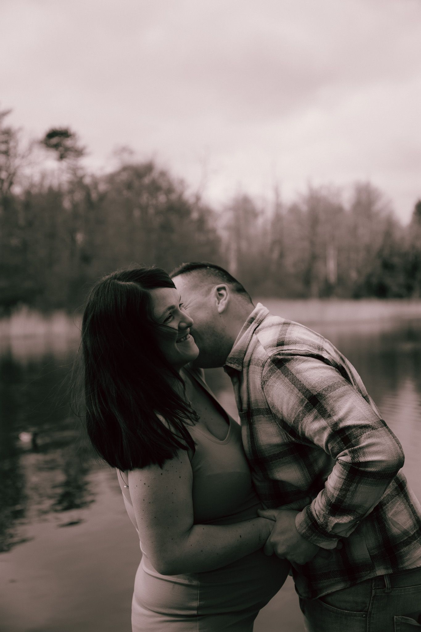 A romantic lake side photo sequence shows a pregnant woman and her husband sharing an intimate moment in black and white tones.