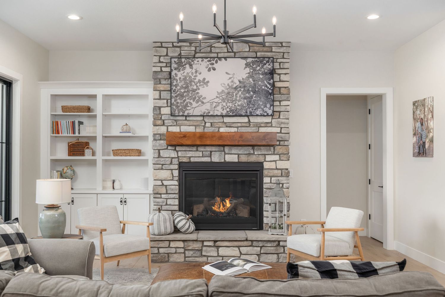 Cozy living room with stone fireplace, built-in shelves, modern chandelier, and neutral decor on hardwood floors.