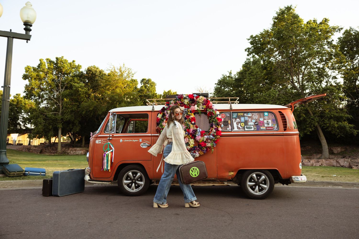 A vintage orange Volkswagen van decorated with floral arrangements parked in a park at sunset.