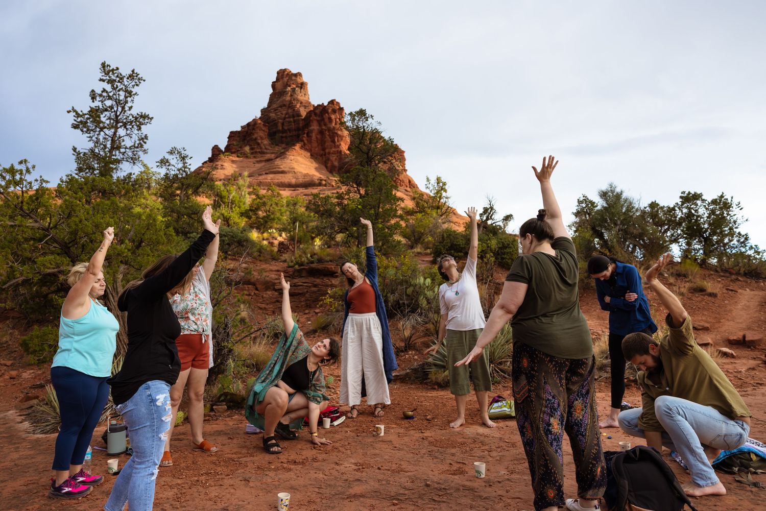 A group of people raise their arms joyfully against the backdrop of Bell Rock in Sedona, Arizona during sunset.
