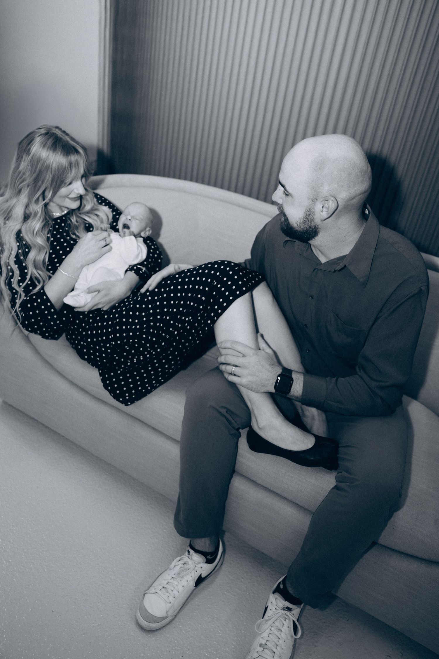 A touching black and white photograph showing a tender family moment with a newborn baby on a couch.